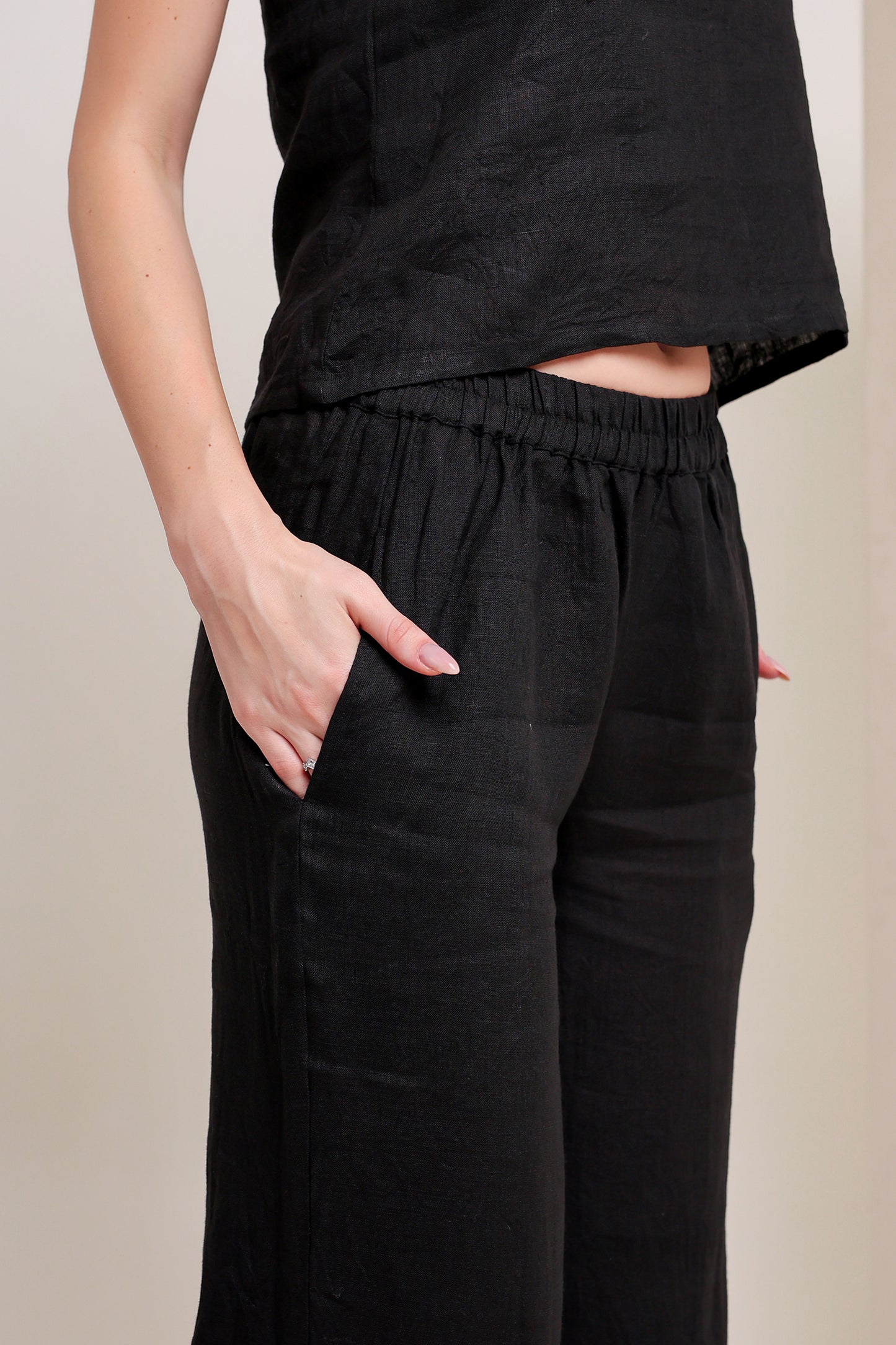 Person wearing a black linen top and pants set against a beige background.