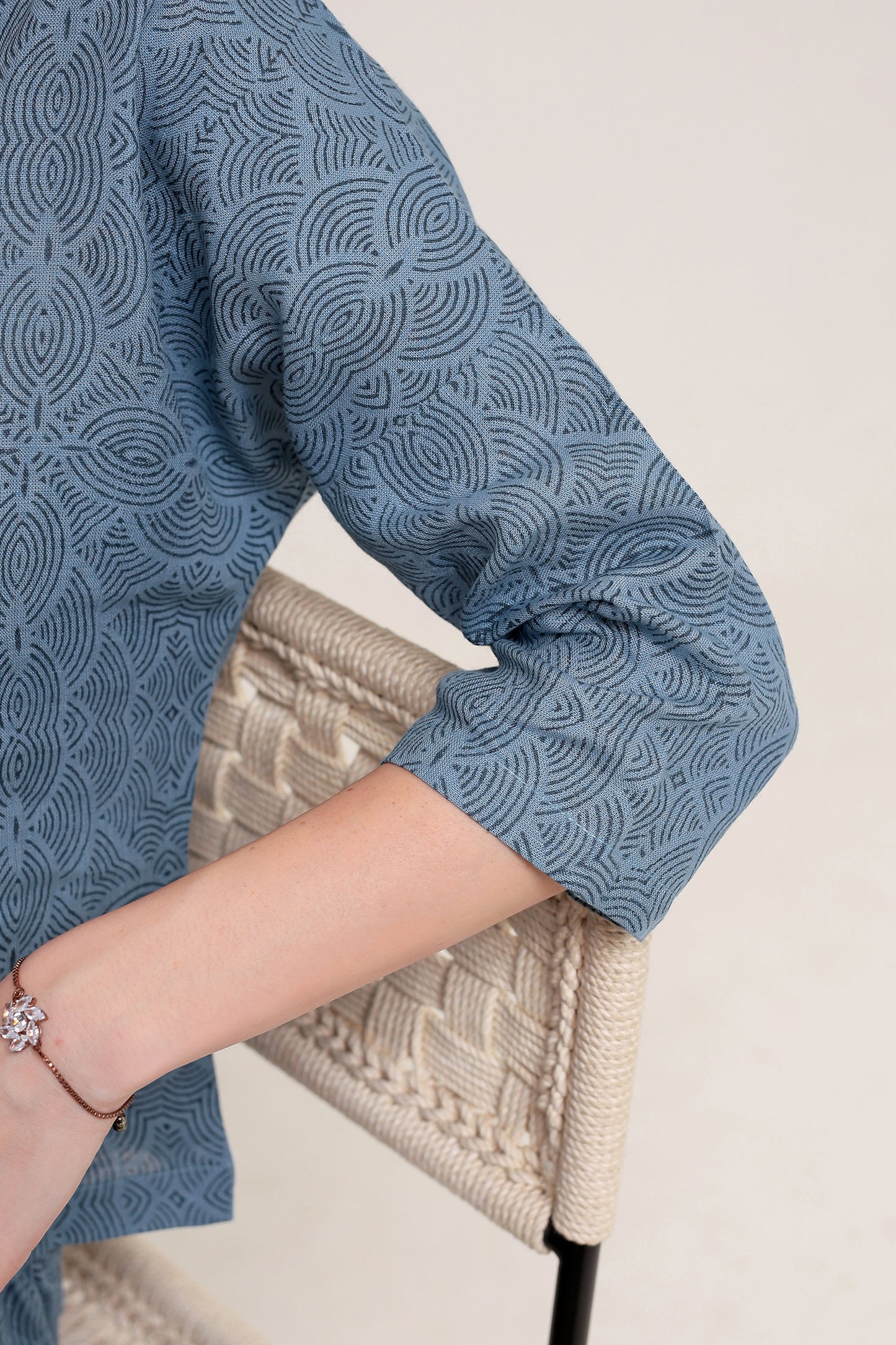Person wearing a blue patterned linen shirt with a beige knitted bag against a light background.