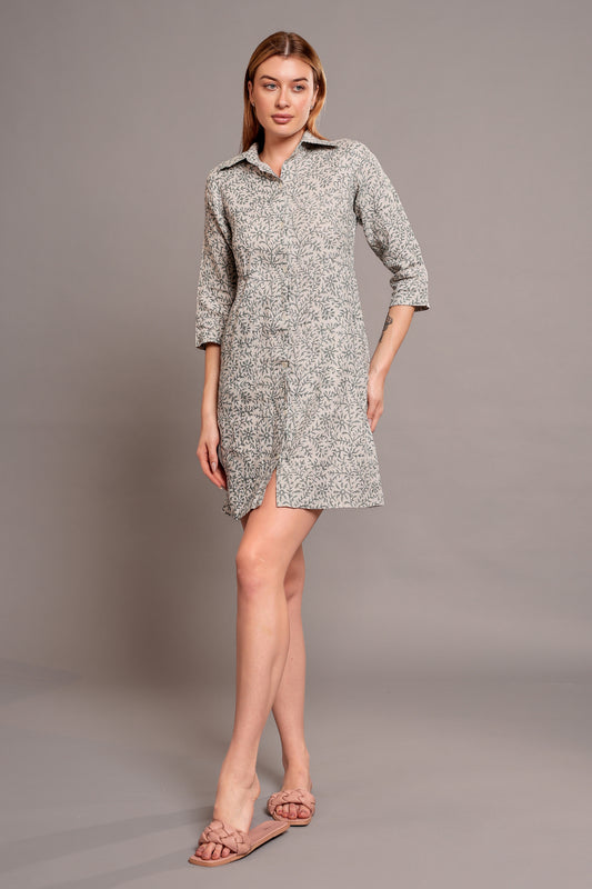 Woman wearing a patterned linen short dress standing against a gray background.