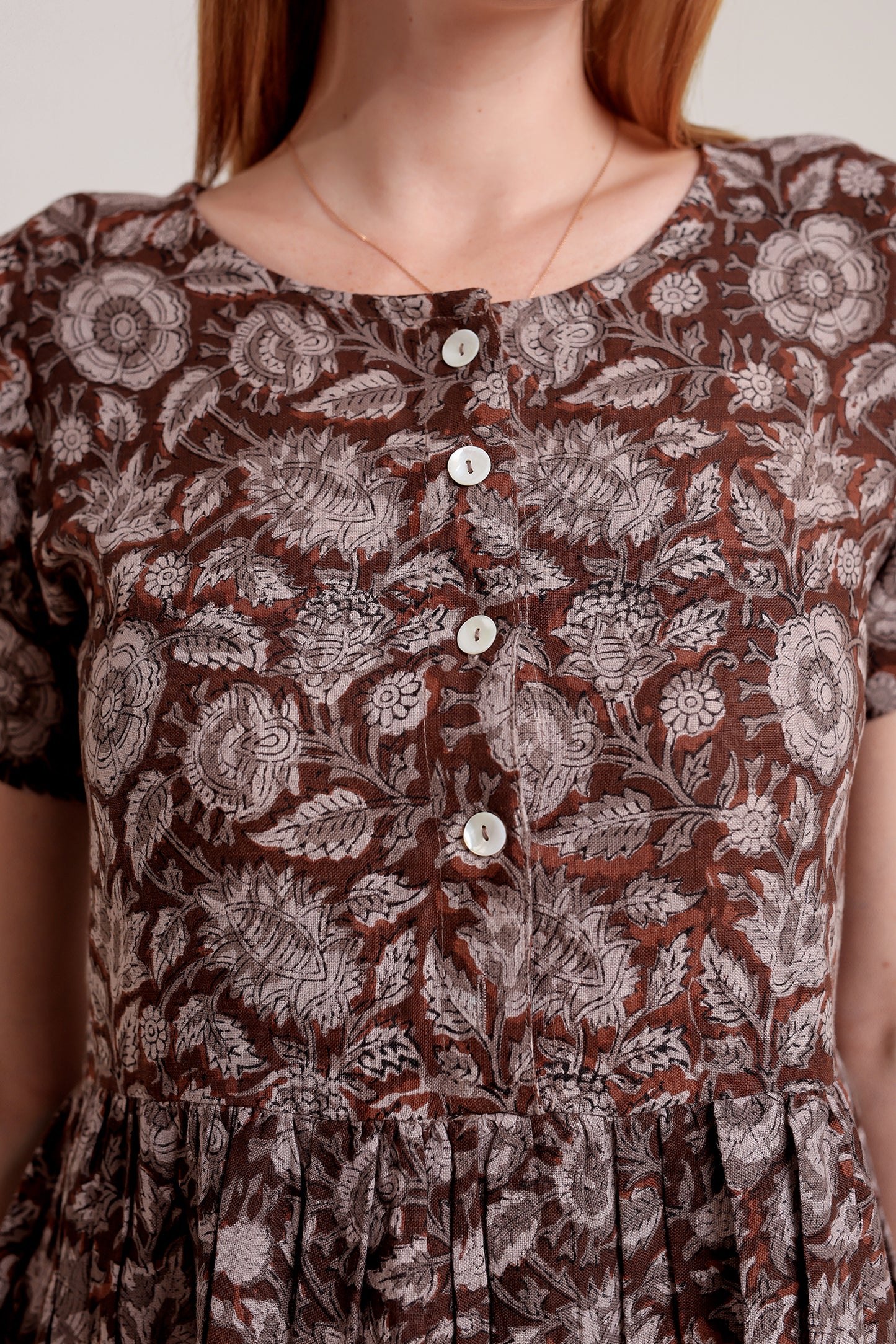 Close-up of a brown floral patterned linen mini dress with buttons against a neutral background.