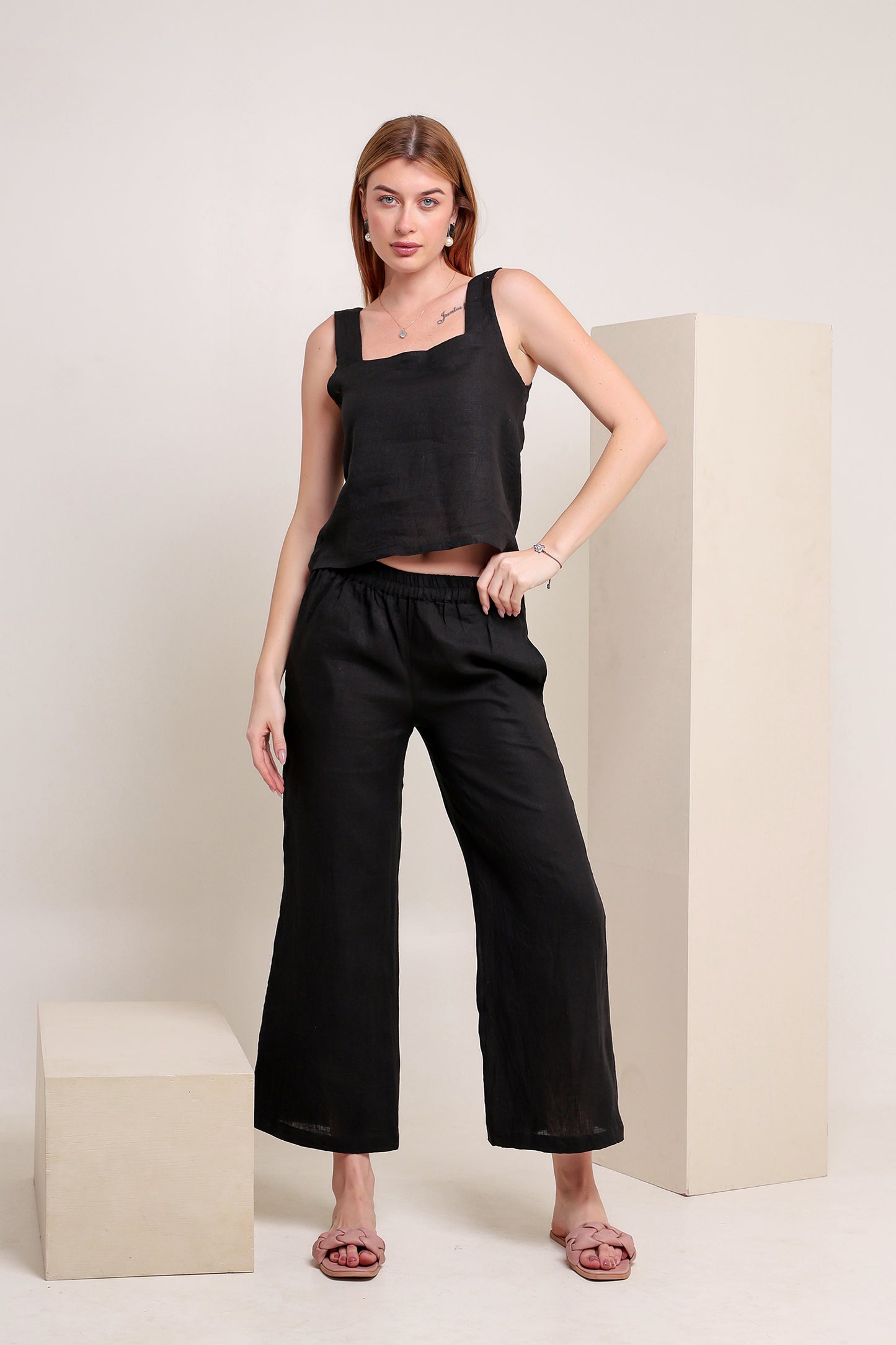 Woman wearing a black linen sleeveless top and pants set against a plain background.