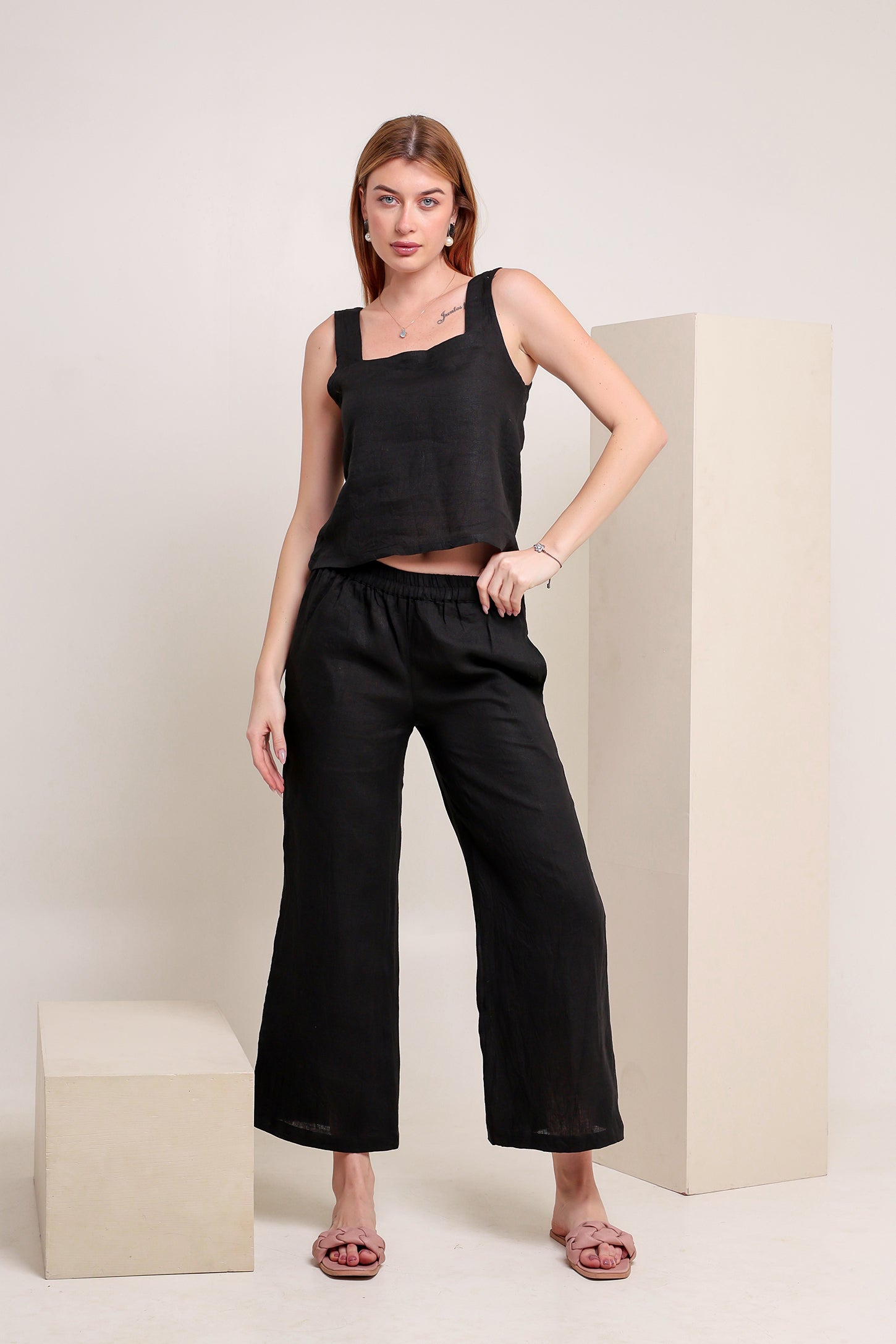 Woman wearing a black linen sleeveless top and pants set against a plain background.