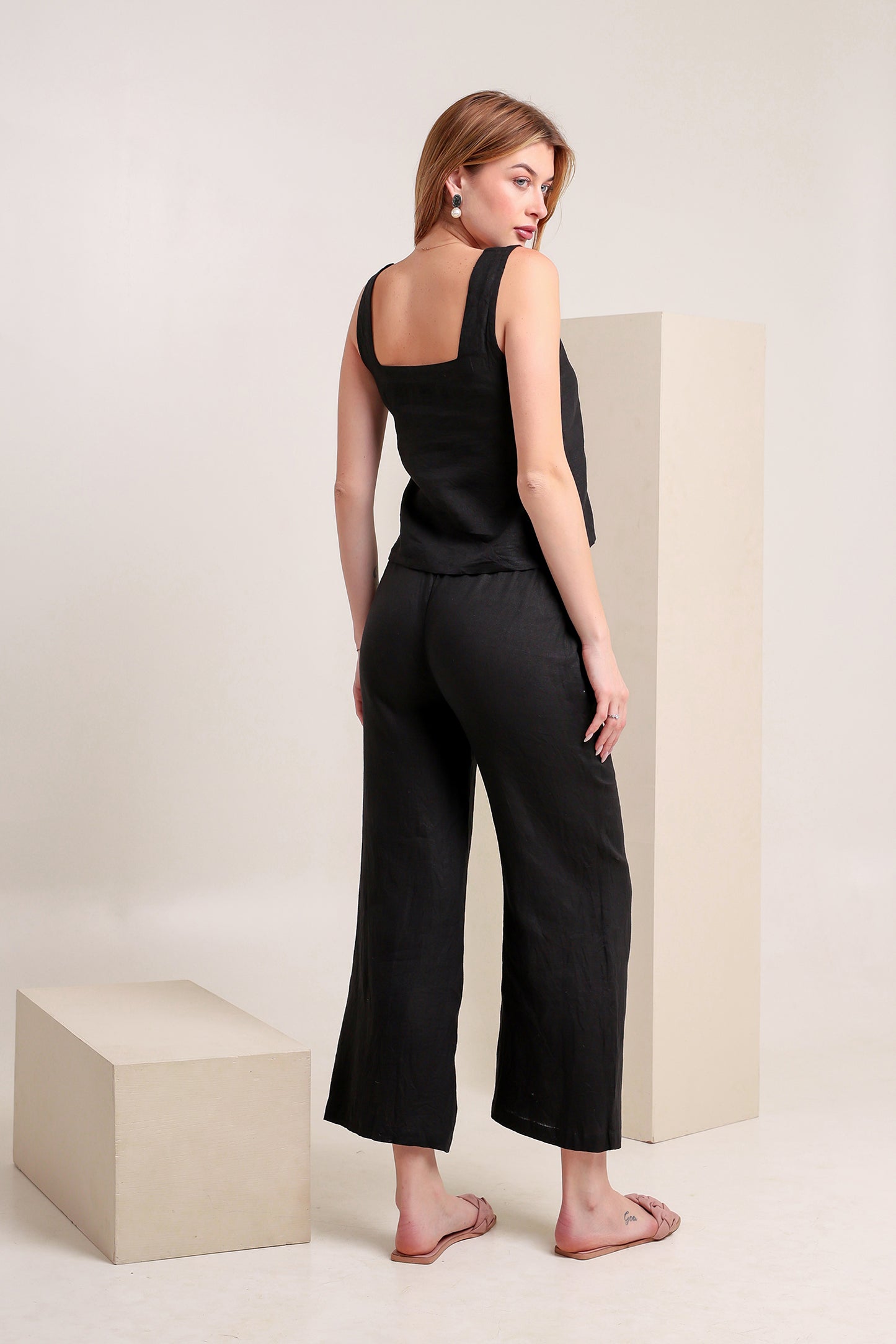 Woman wearing a black linen sleeveless top and pants set in a minimalistic setting.