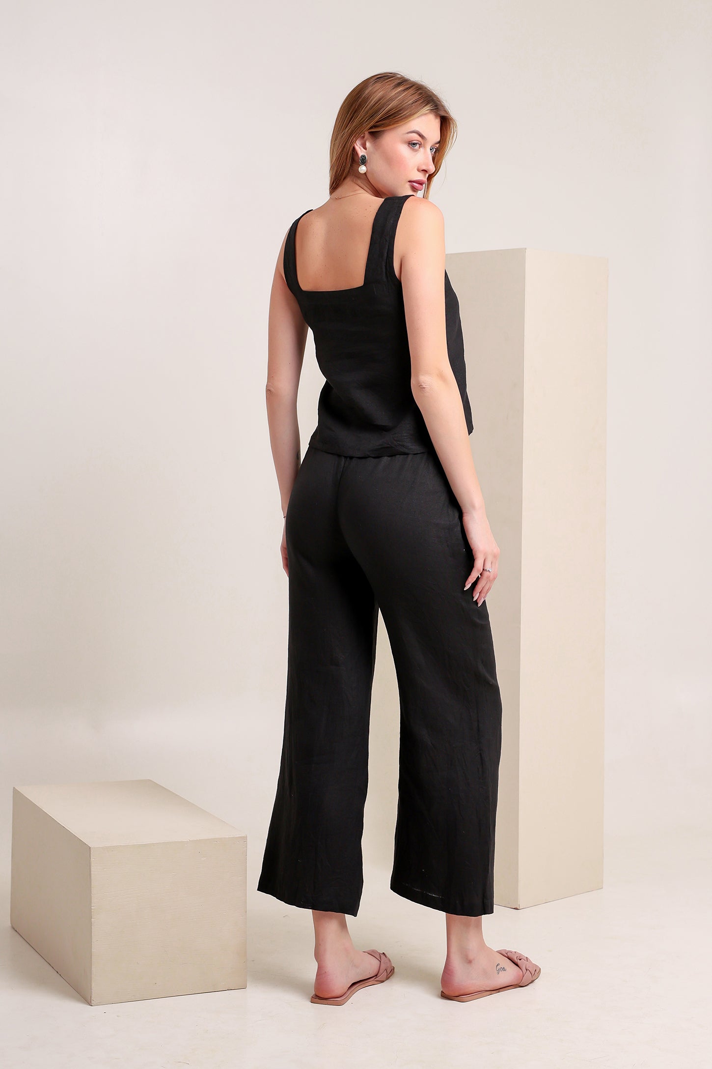 Woman wearing a black linen sleeveless top and pants set in a minimalistic setting.