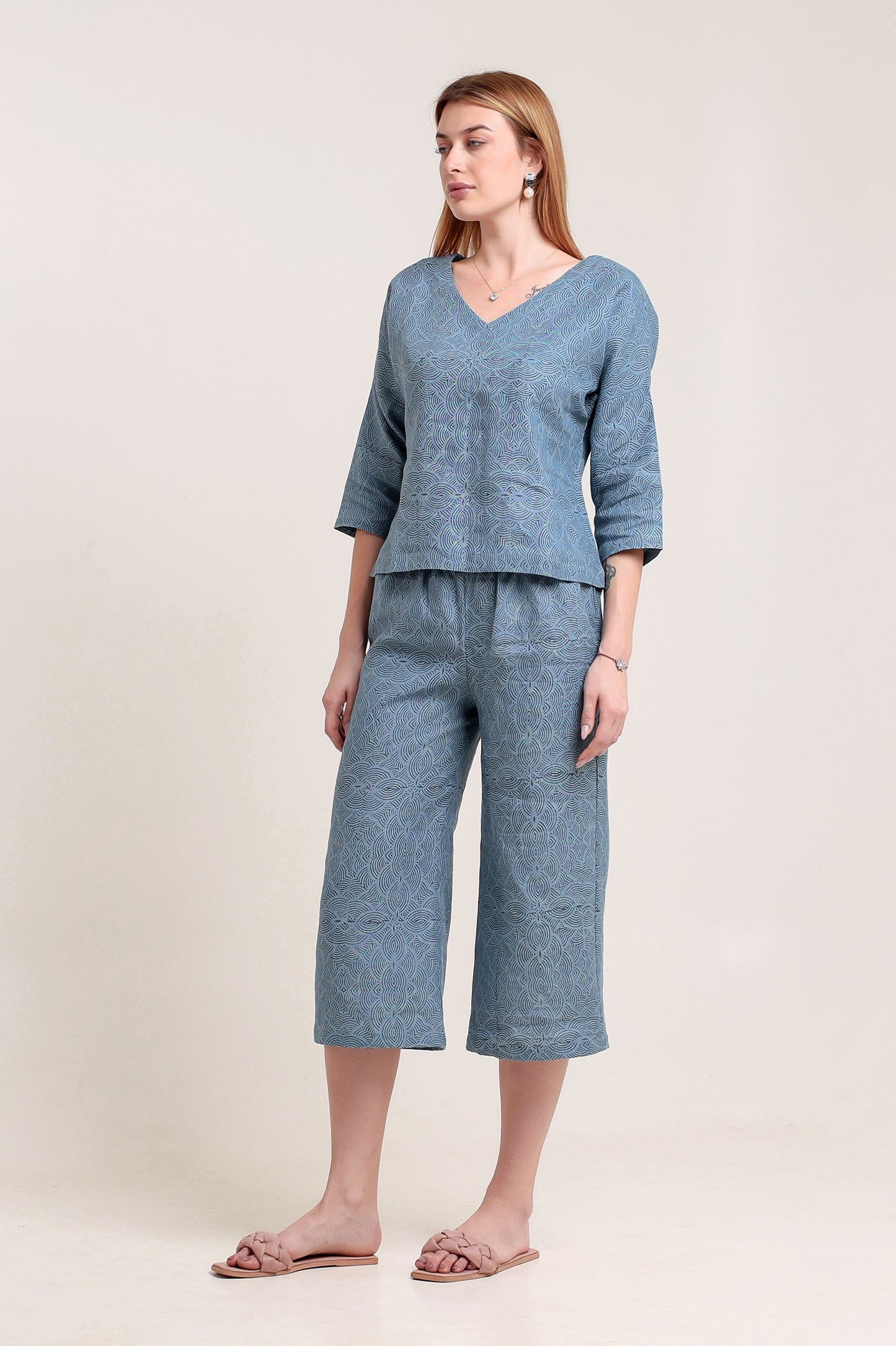 Woman wearing a blue linen top and pants set with wide-leg pants against a plain background.