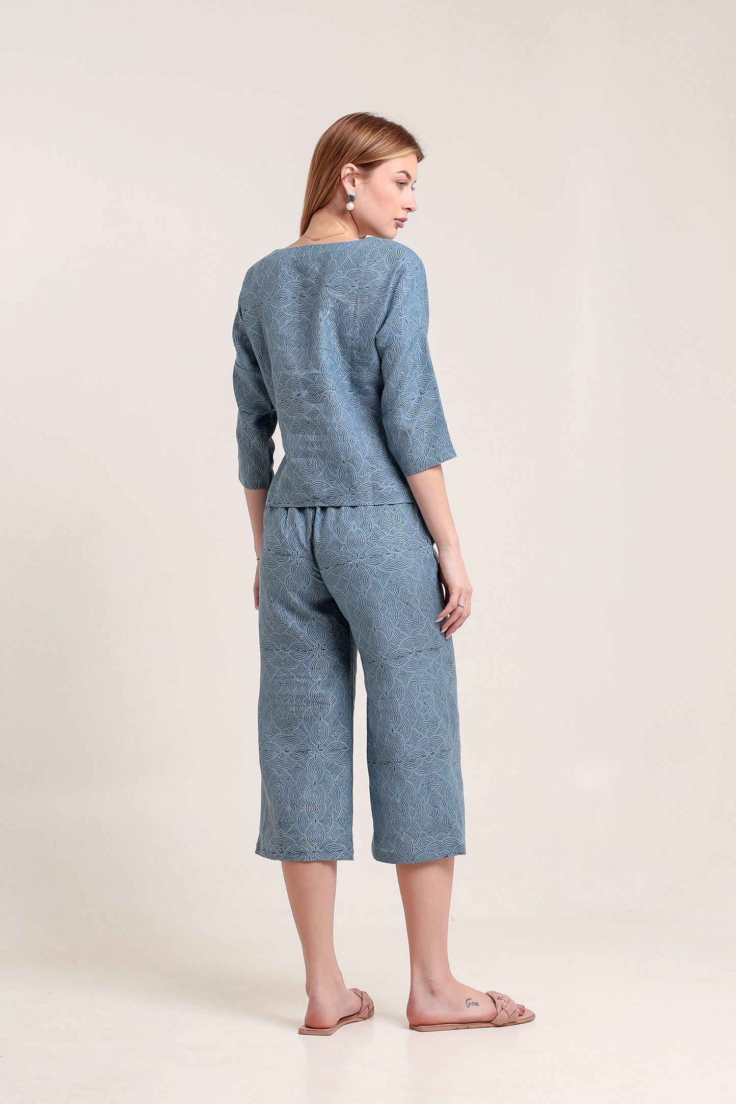 Woman wearing a blue matching linen top and pants set  against a white background.