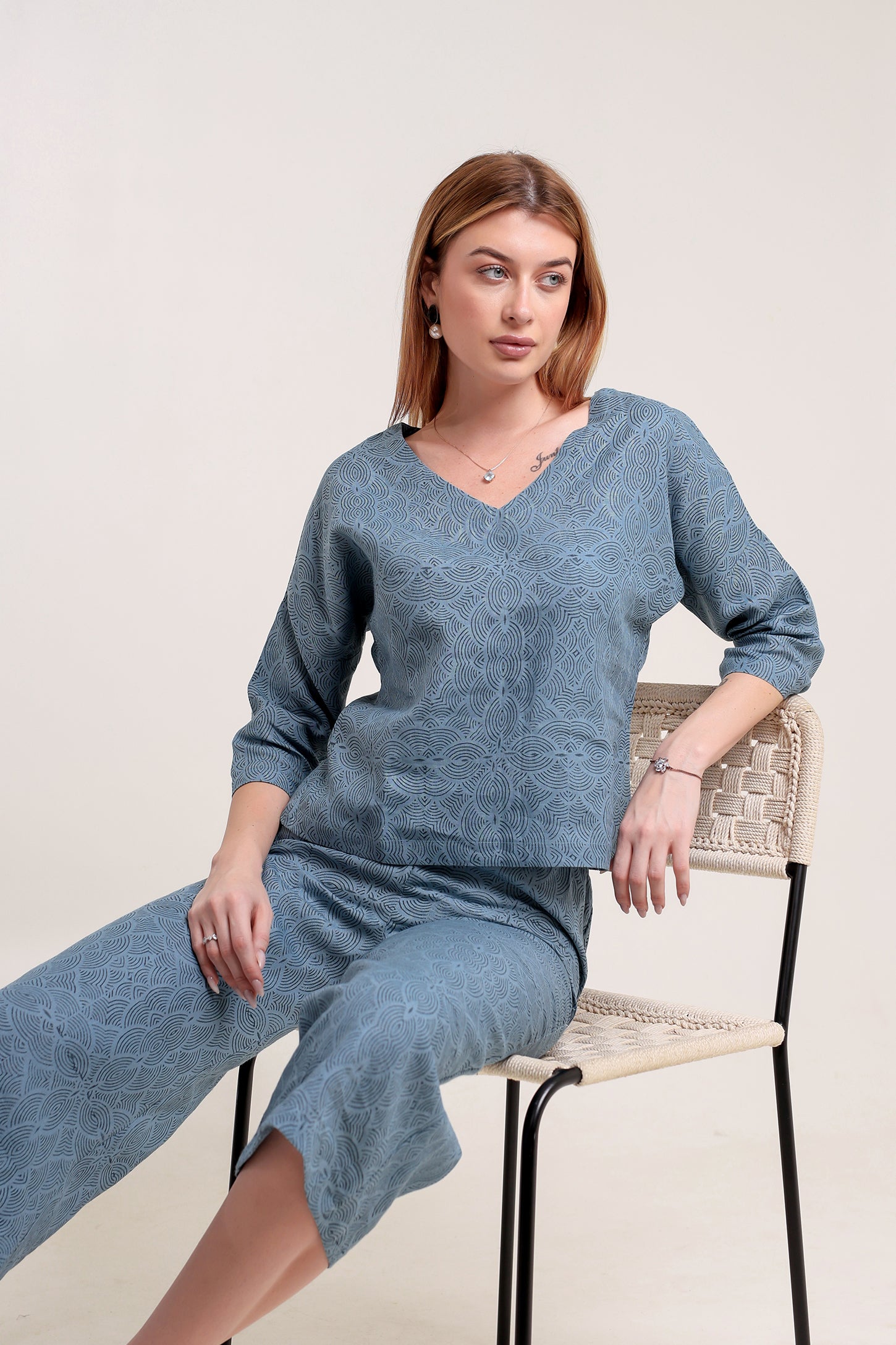 Woman wearing a blue linen top and pants set sitting on a chair against a plain background.