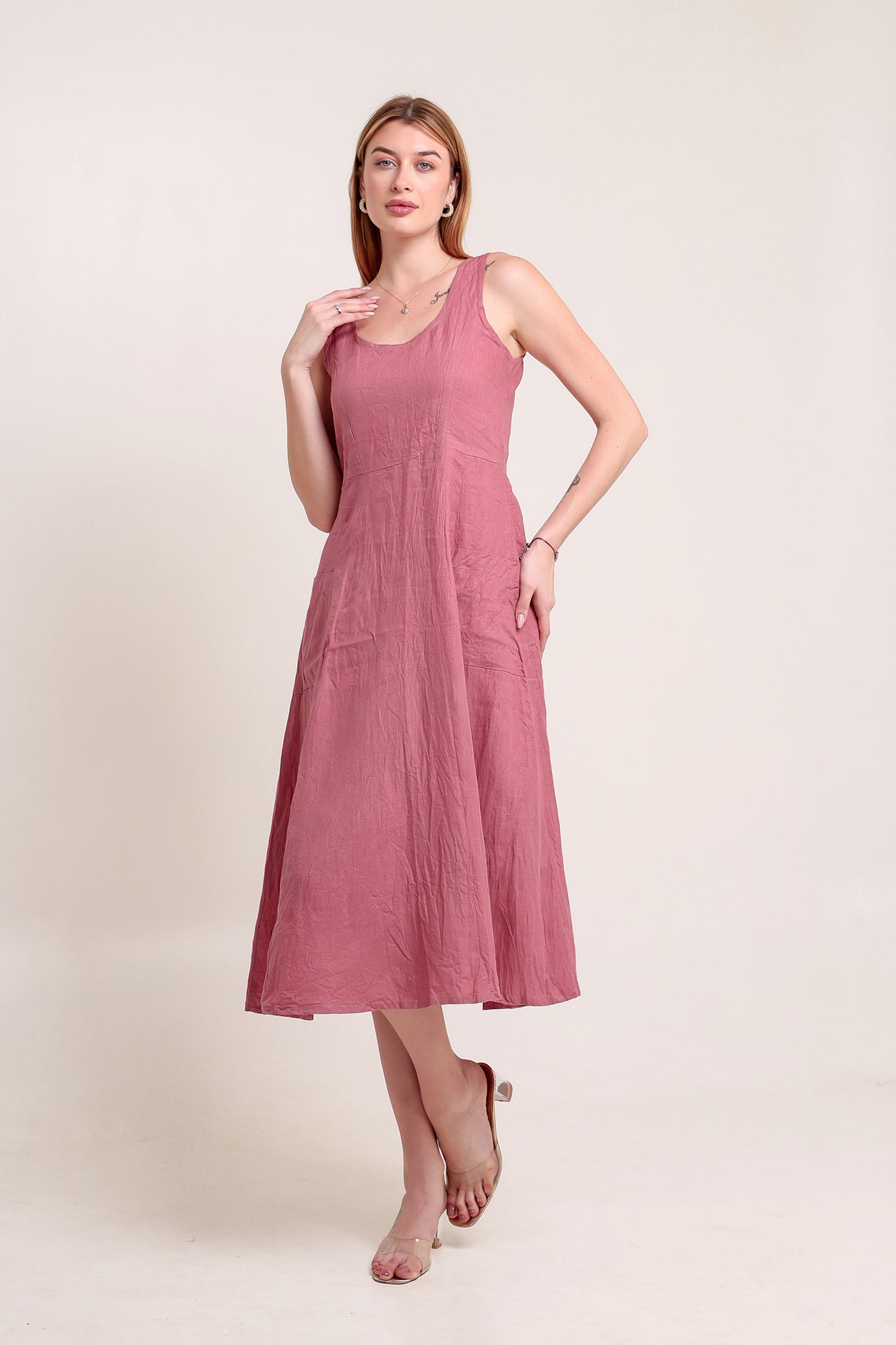 Woman wearing a pink sleeveless linen midi dress against a beige background.