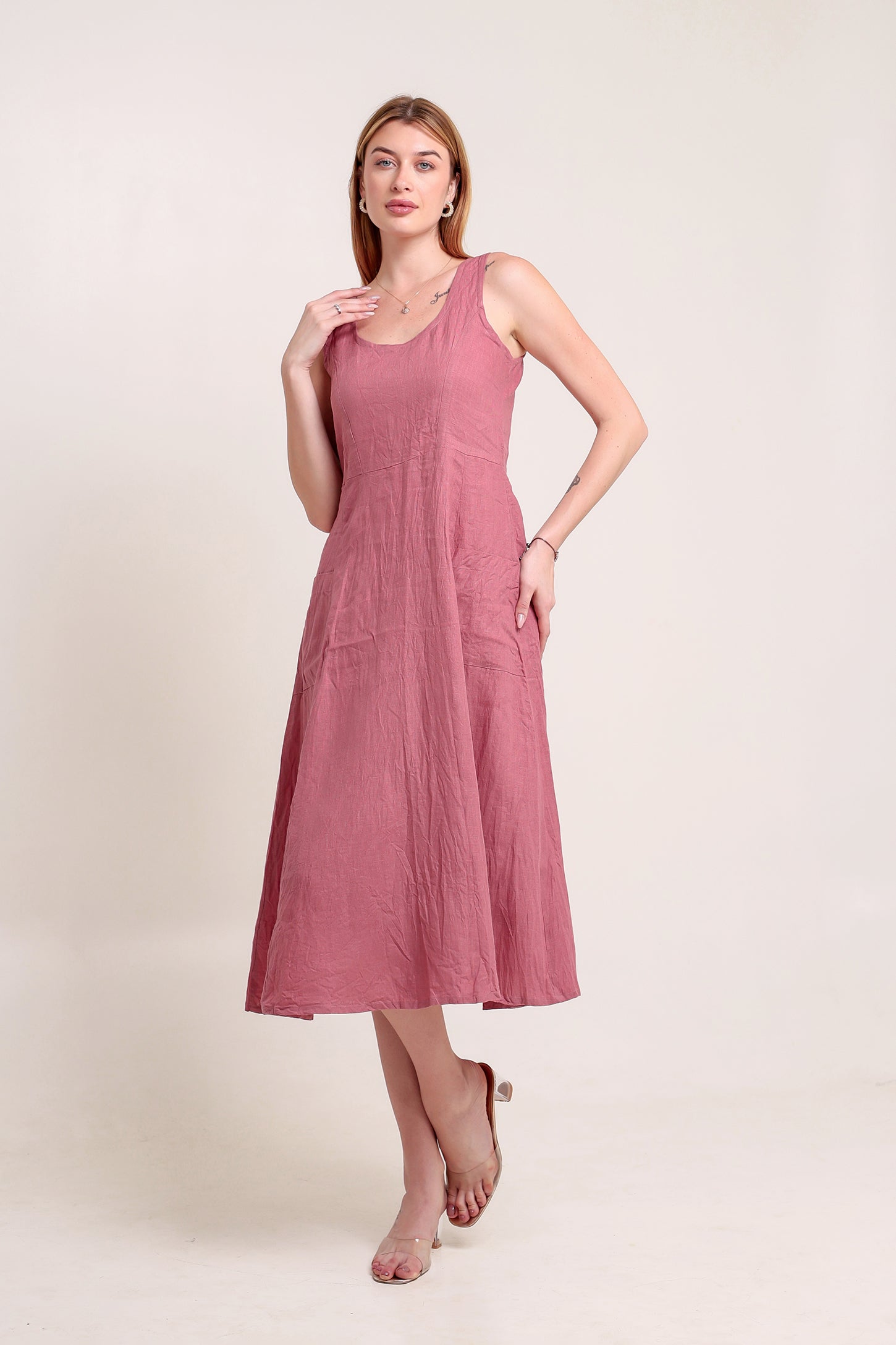 Woman wearing a pink sleeveless linen midi dress against a beige background.