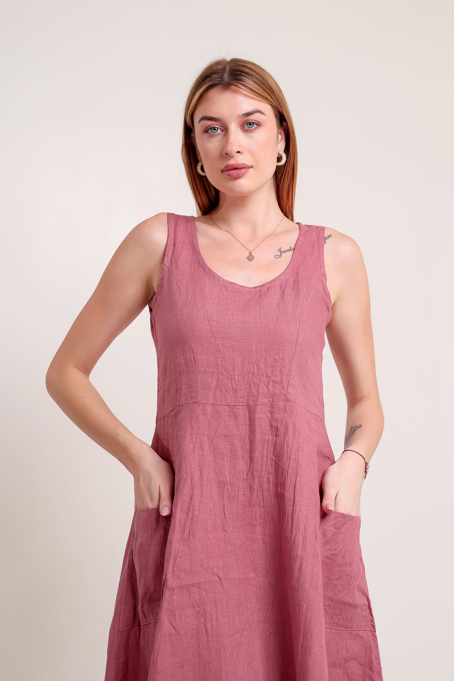 Woman wearing a sleeveless pink linen midi dress against a plain background.