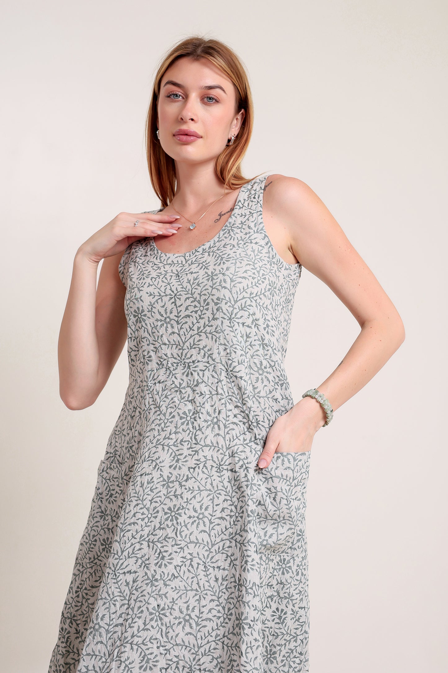 Woman wearing a sleeveless floral linen floral maxi dress against a plain background.
