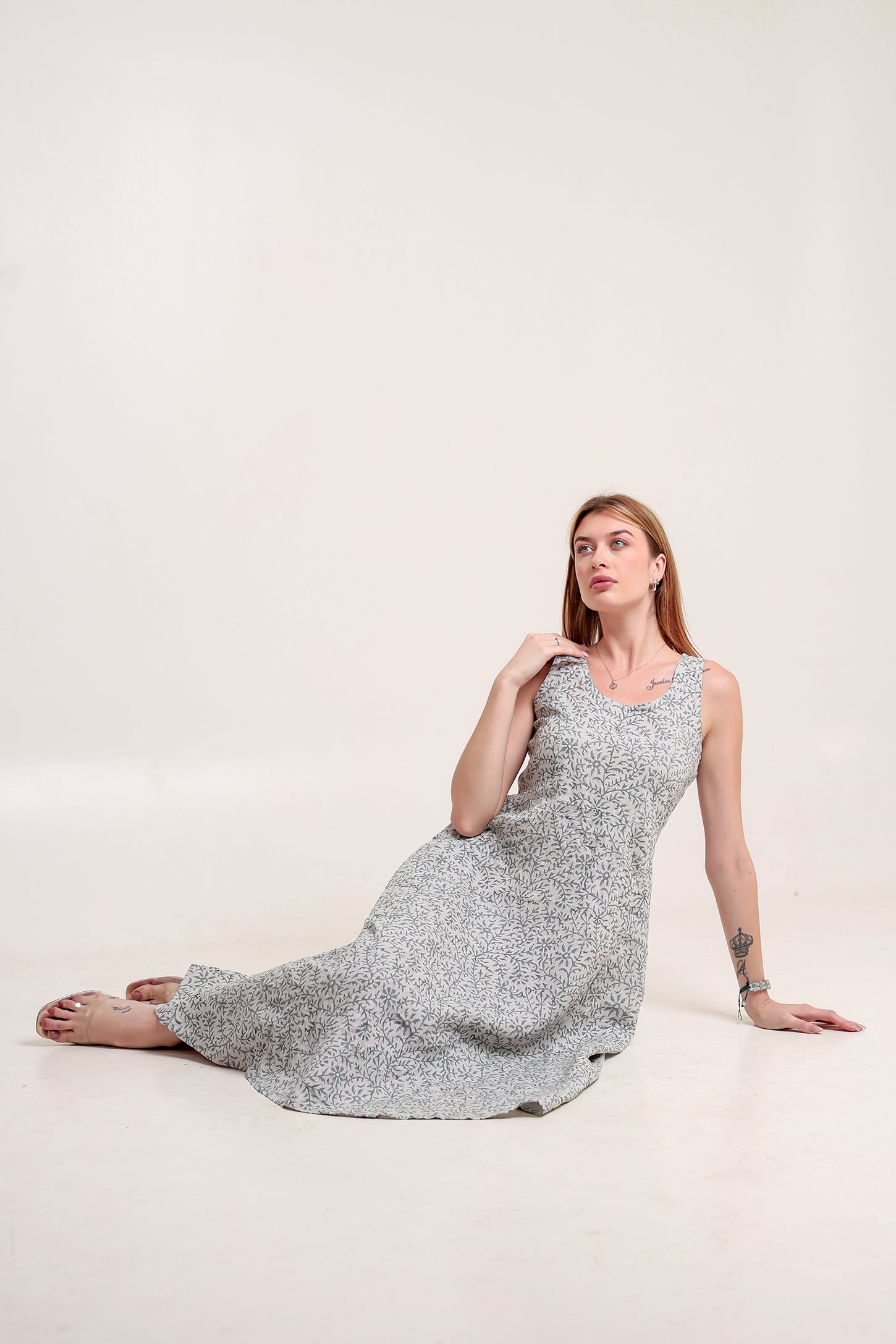 Woman wearing a sleeveless floral linen floral maxi dress against a plain background.