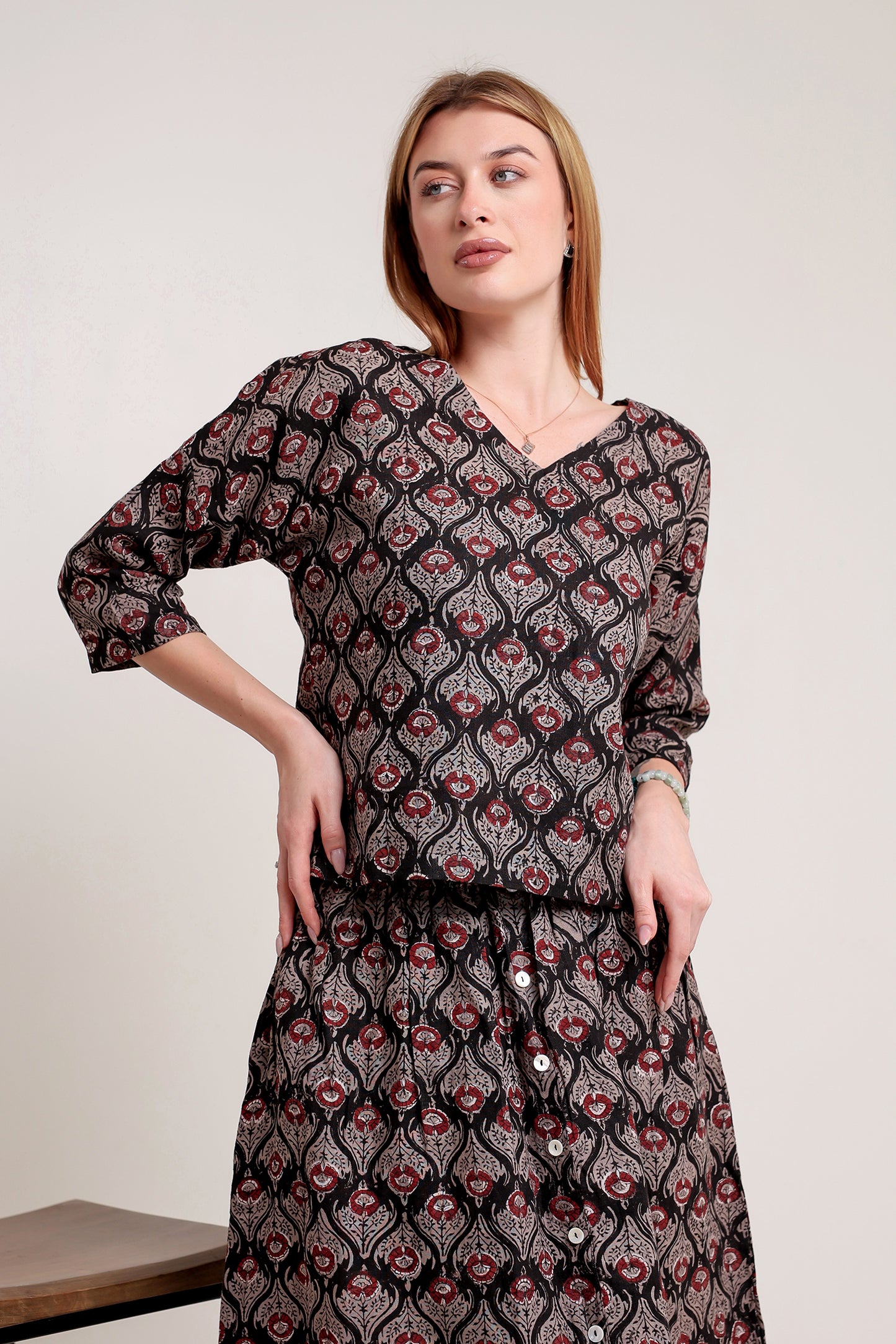 Woman wearing a stylish linen skirt and top set with patterns against a plain background.