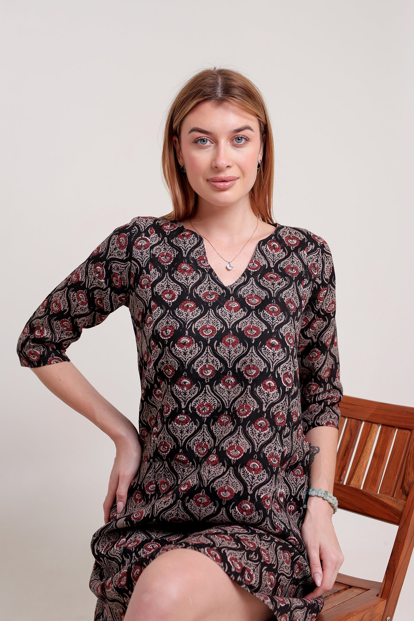 Woman wearing a patterned linen mini dress sitting on a chair against a plain background.