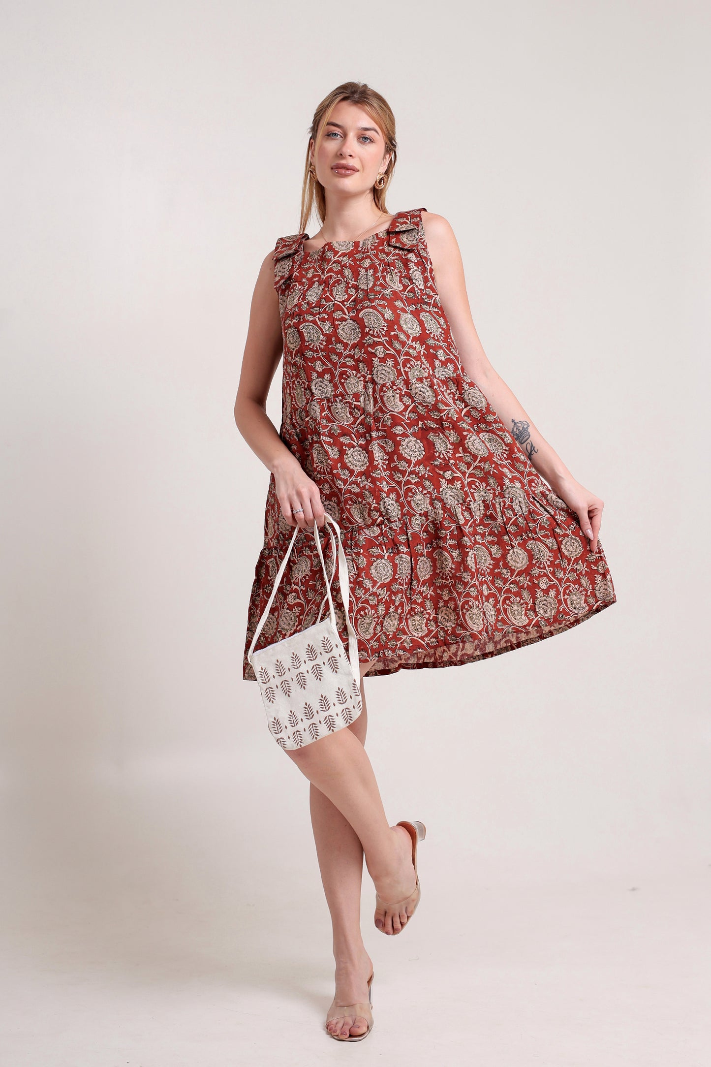 Woman wearing a red patterned linen floral mini dress holding a matching handbag against a white background.