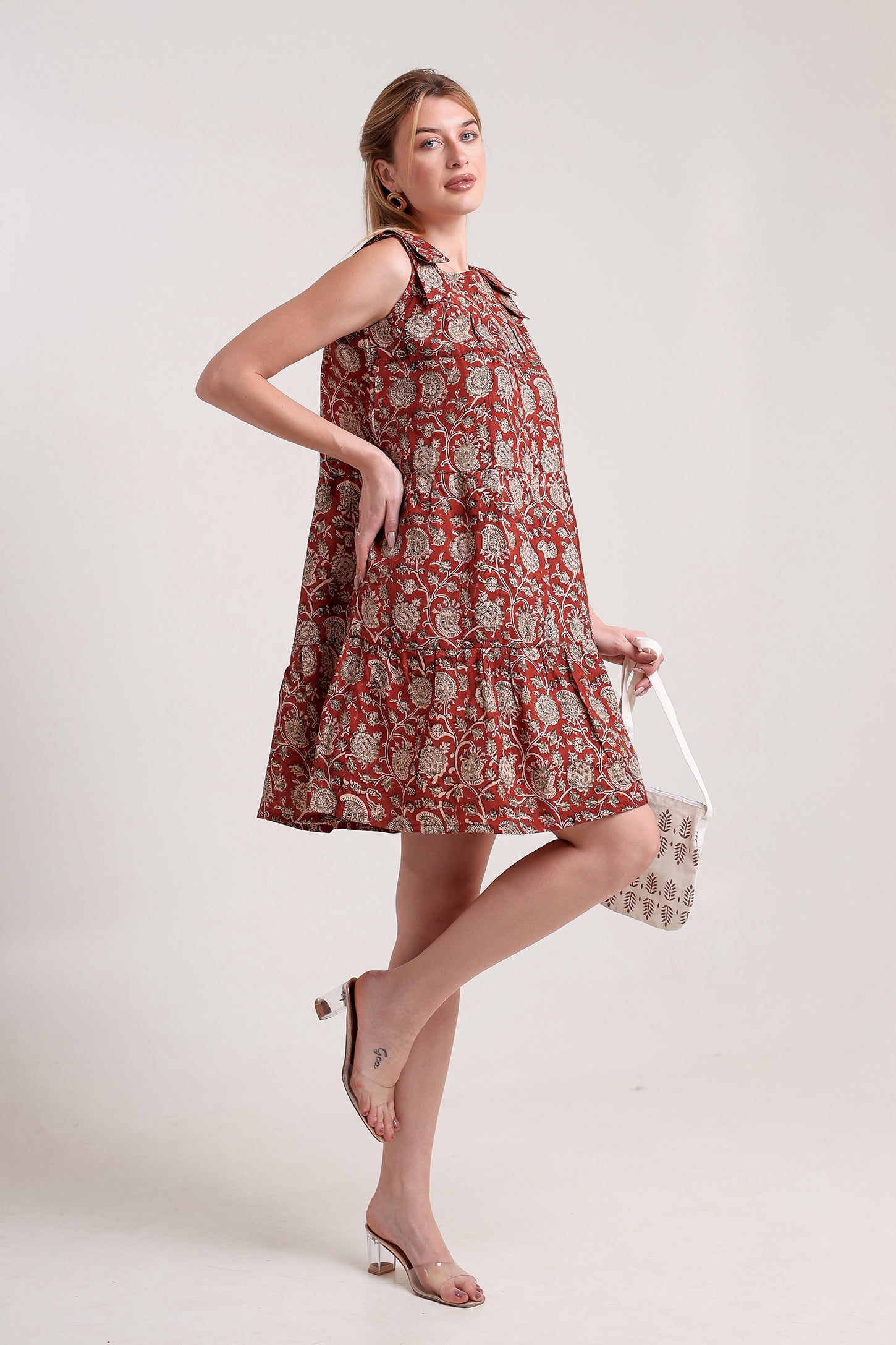 Woman wearing a patterned linen floral mini dress holding a clutch against a plain background.