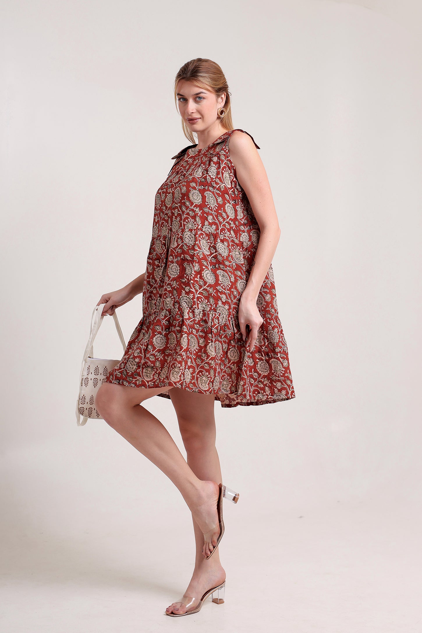 Woman wearing a red floral linen floral mini dress holding a white bag against a light background.