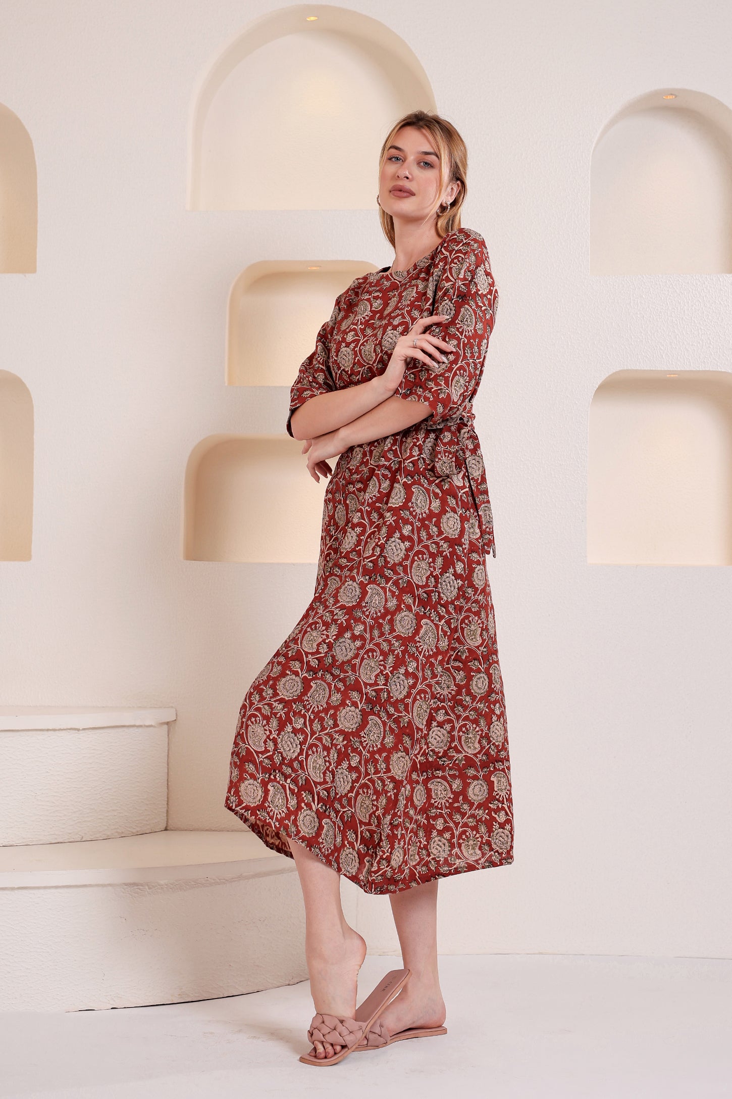 Woman wearing a red floral linen floral maxi dress standing in a modern indoor setting with white walls and geometric light fixtures.