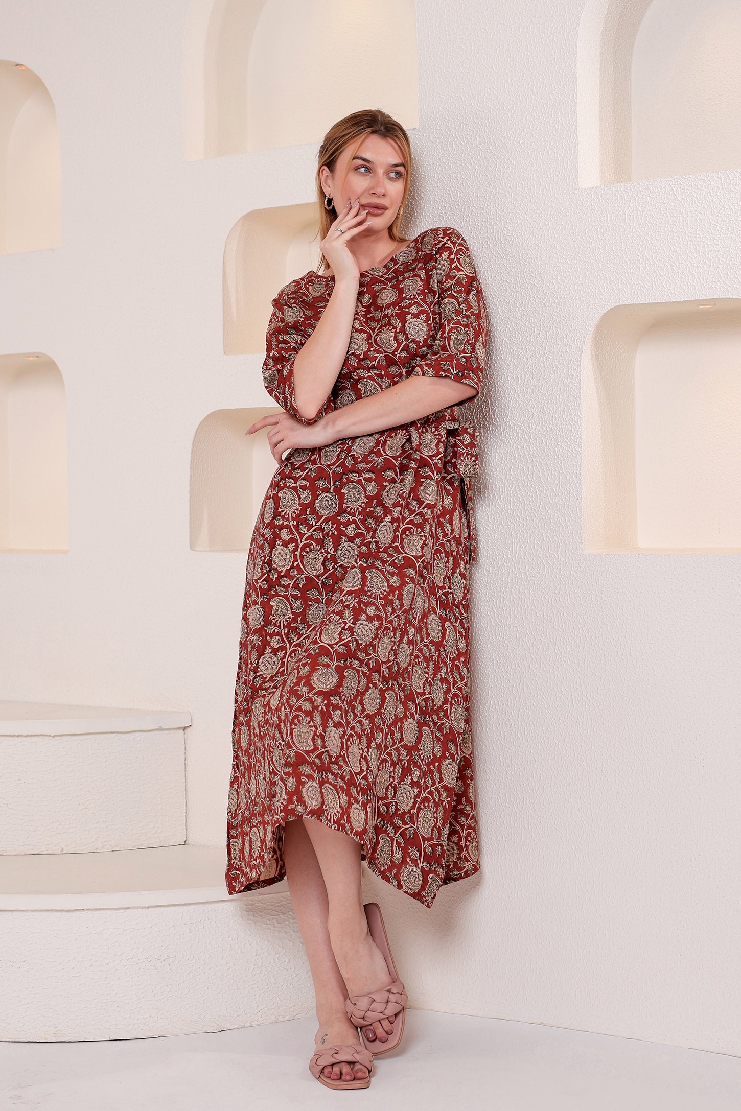 Woman wearing a red patterned linen floral maxi dress sitting on a white chair in a minimalistic setting.