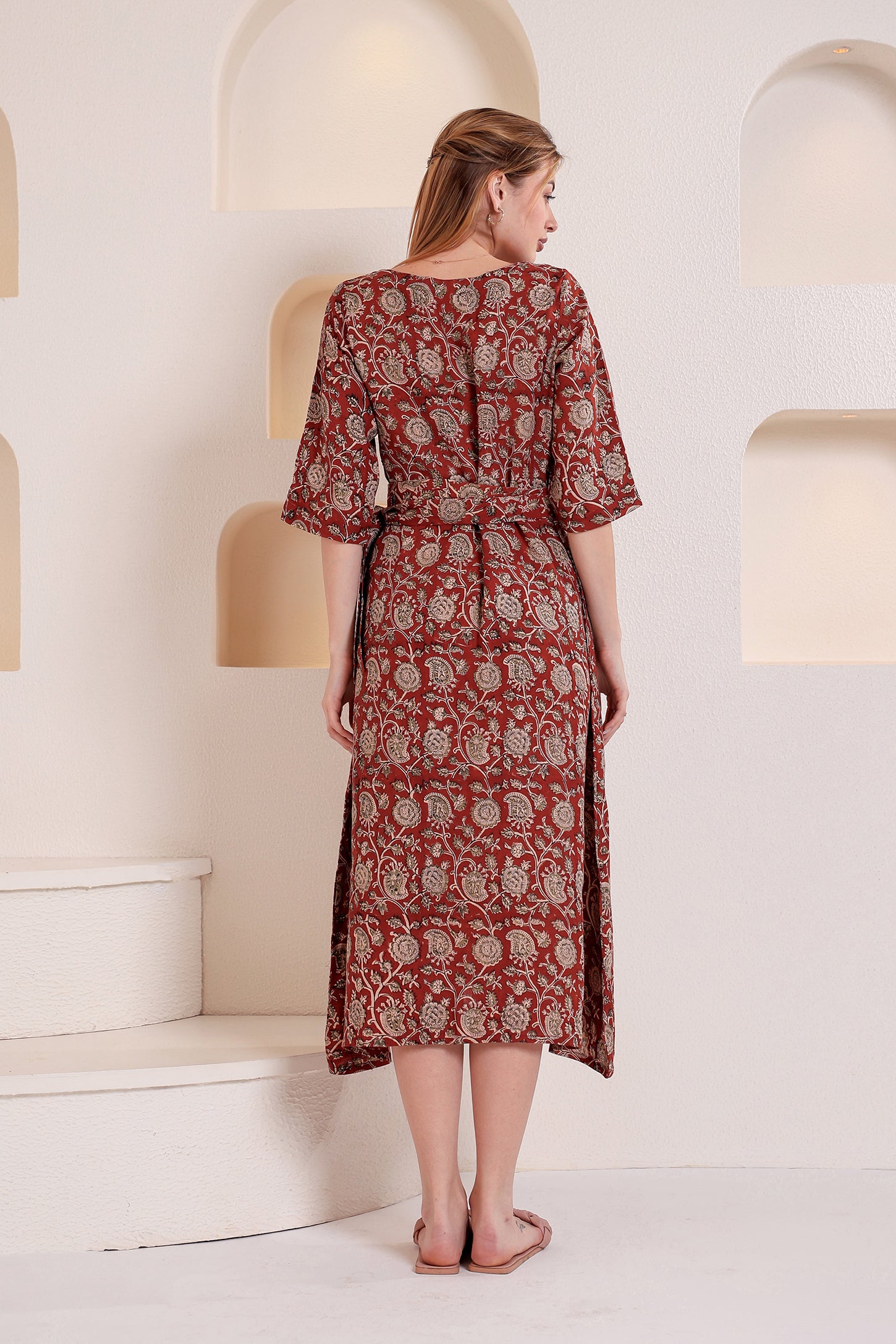 Woman wearing a red patterned linen floral maxi dress standing in a minimalistic room with white walls and a light-colored floor.