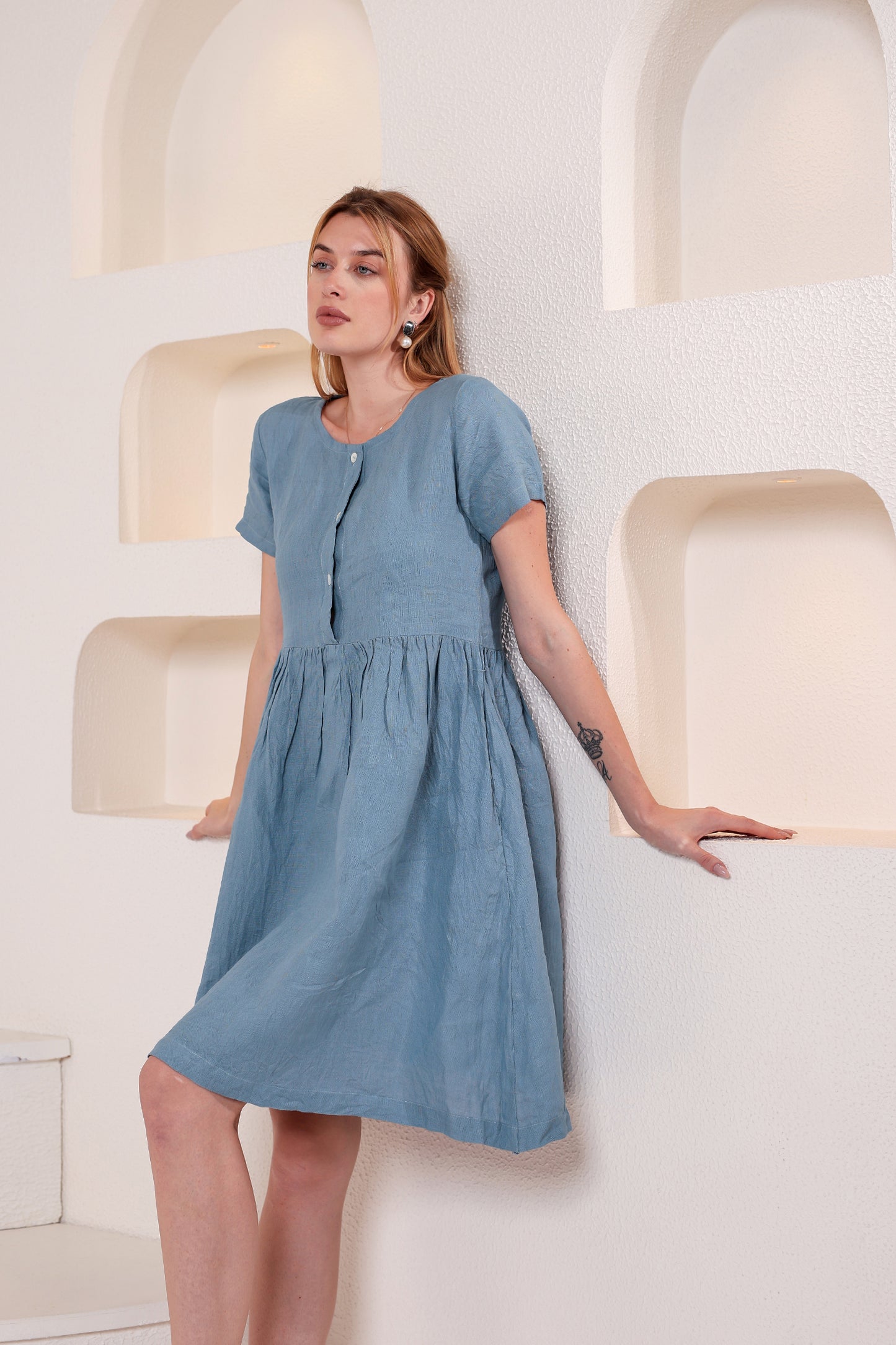 Woman wearing a blue linen midi dress against a light-colored wall.