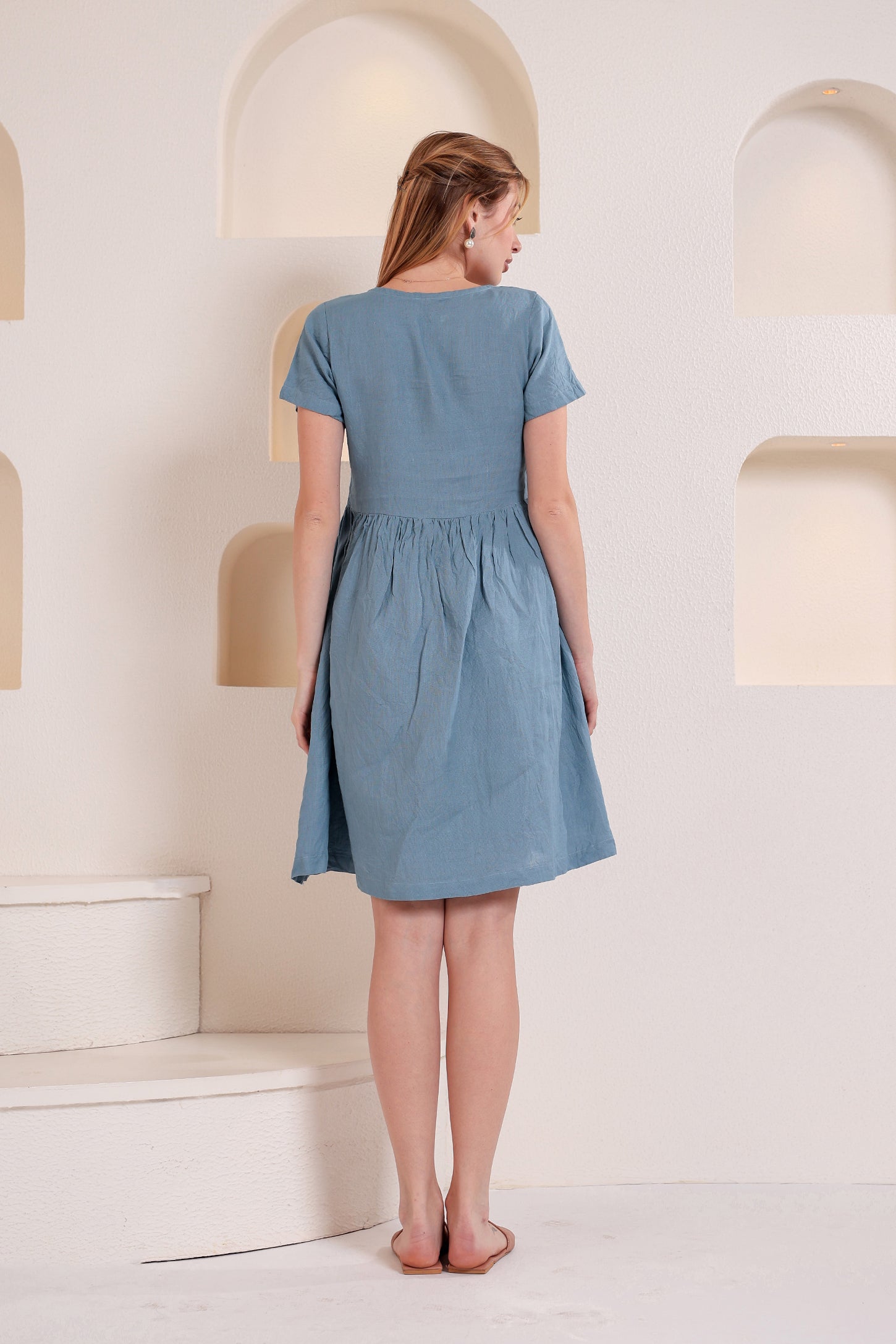 Woman wearing a blue linen midi dress standing on a white staircase against a light-colored wall.