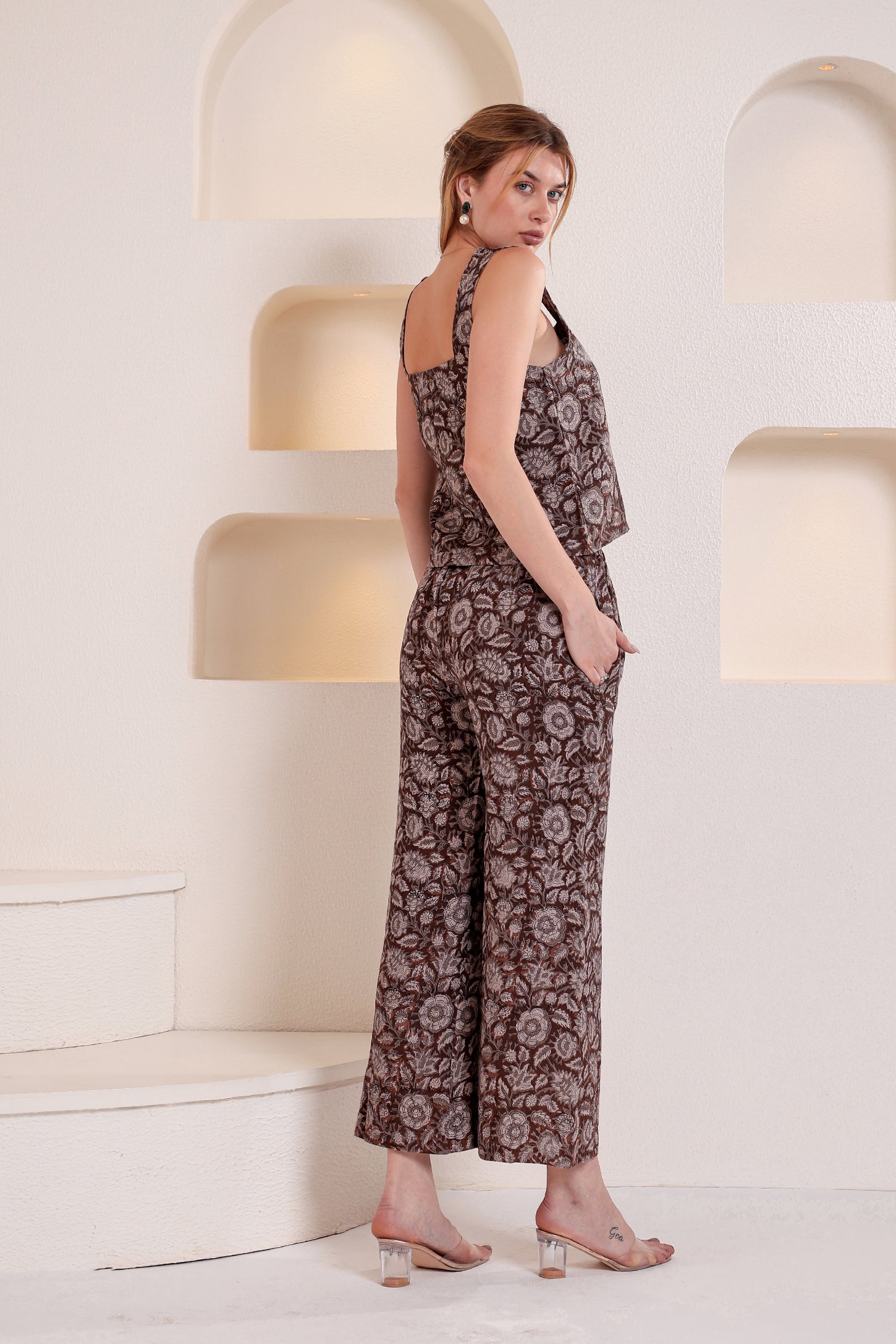 Woman wearing a patterned linen jumpsuit standing in a modern interior setting.