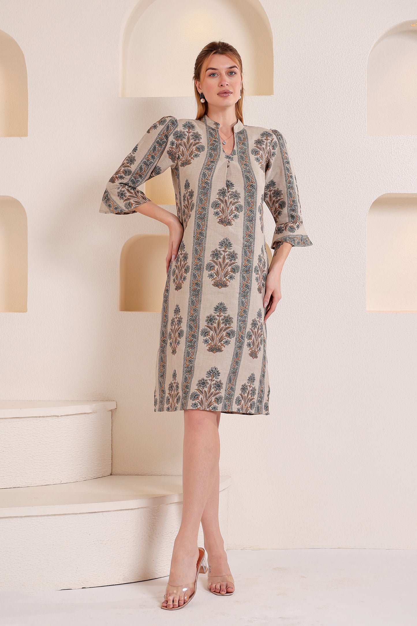 Woman wearing a patterned linen midi dress standing in a softly lit room with geometric arches.