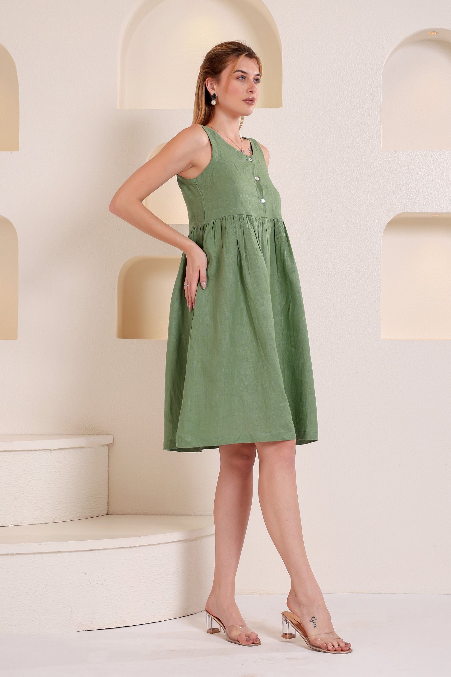 Woman wearing a green linen mini dress standing in a minimalistic setting with white walls and a light-colored floor.