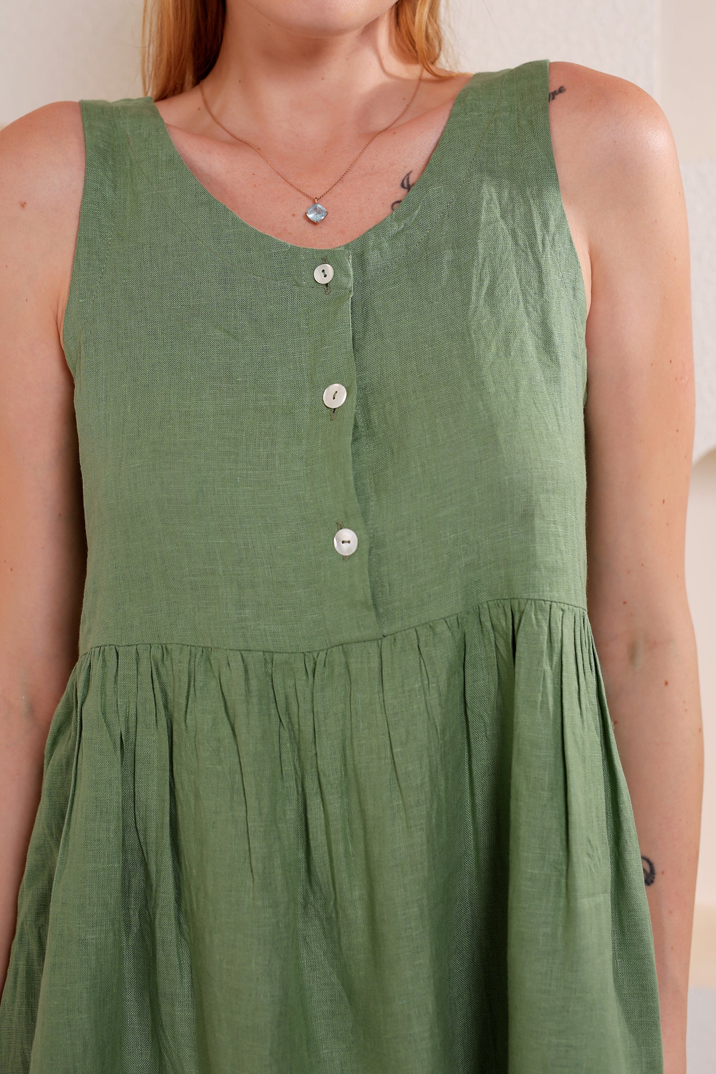 Green sleeveless dress with buttons on a plain background