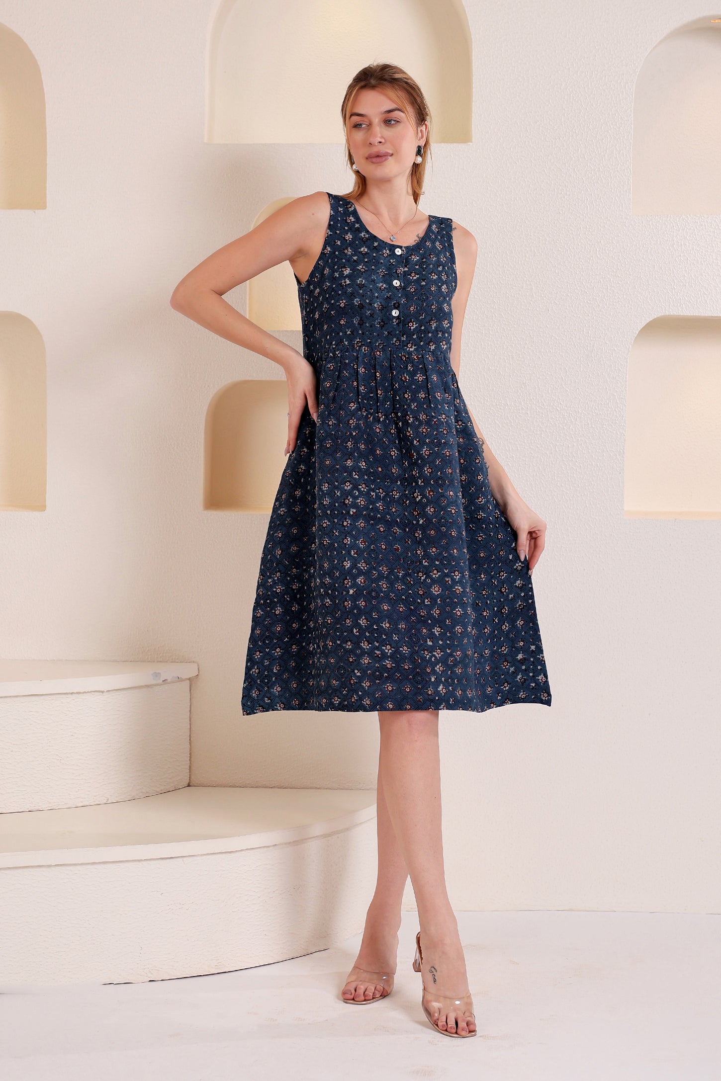 Woman wearing a navy blue dress with white patterns, showcasing a sleeveless linen floral midi dress in a minimalistic setting.