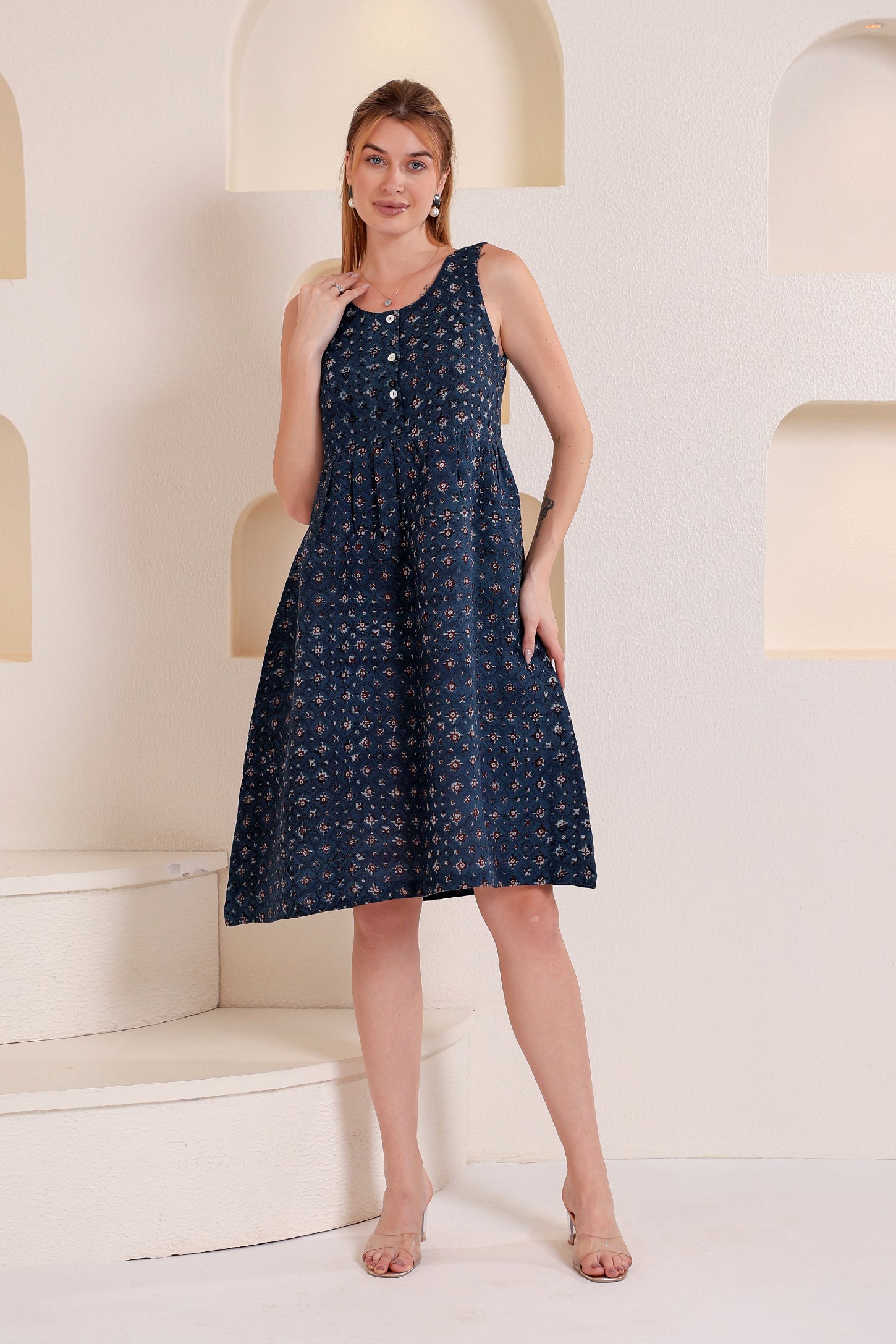 Woman wearing a navy blue dress with white patterns in a sleeveless linen floral midi dress style within a minimalistic setting.
