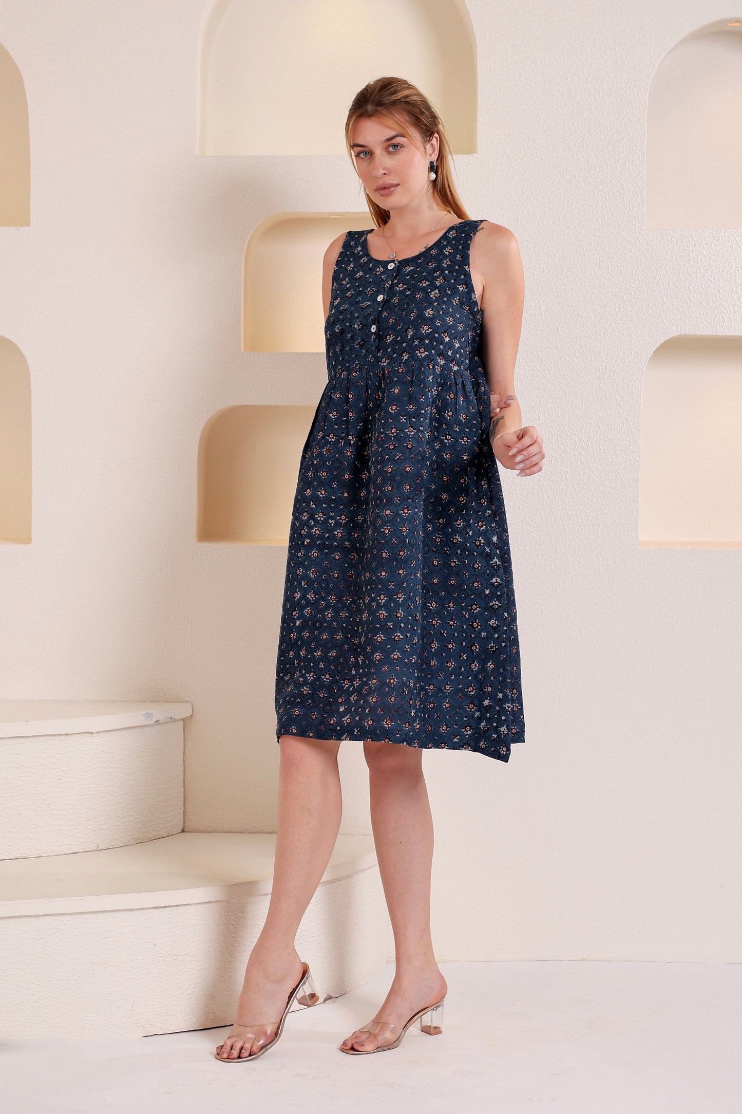Woman wearing a navy blue dress with white patterns, styled as a sleeveless linen floral midi dress in a minimalistic setting.