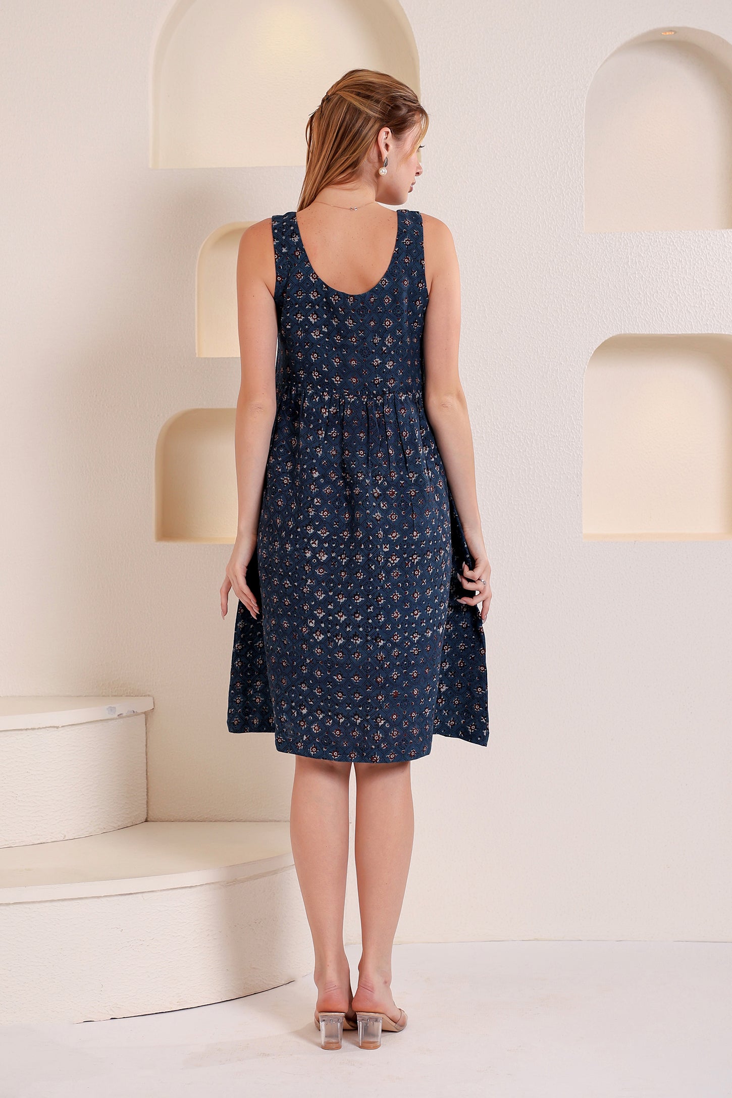 Woman wearing a navy blue patterned sleeveless linen floral midi dress in a minimalistic setting.