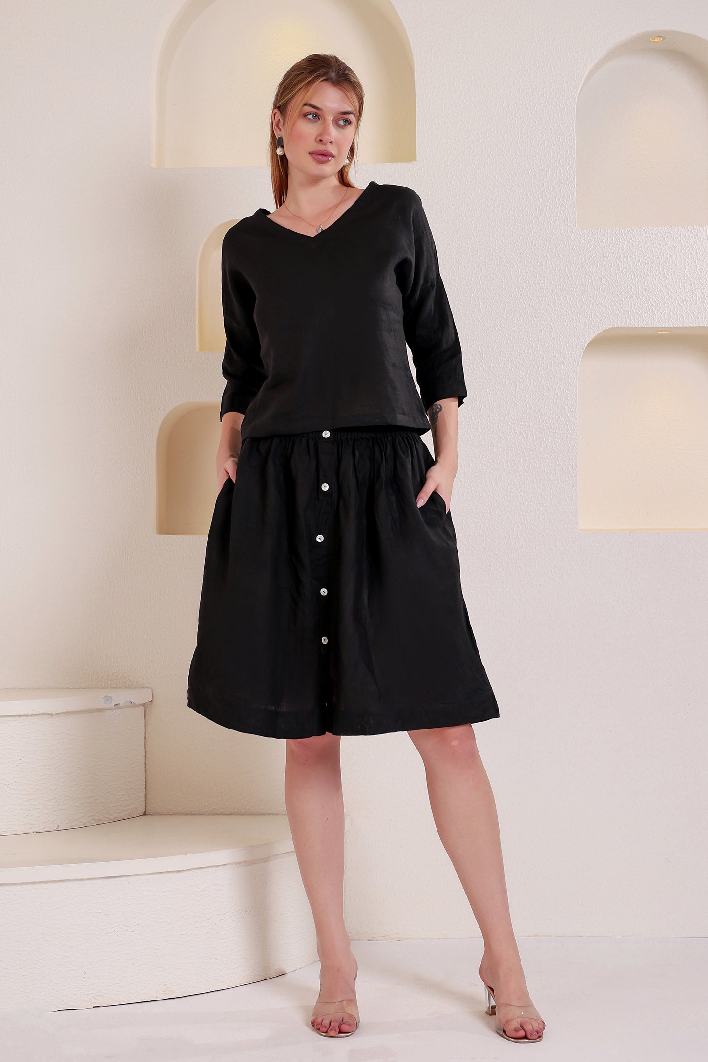 Woman wearing a black buttoned linen top and skirt set standing in a minimalistic setting.