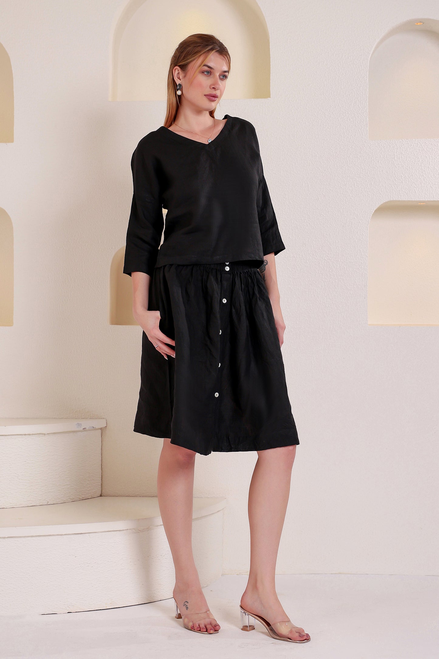 Woman wearing a black buttoned linen top and skirt set in a minimalistic setting.