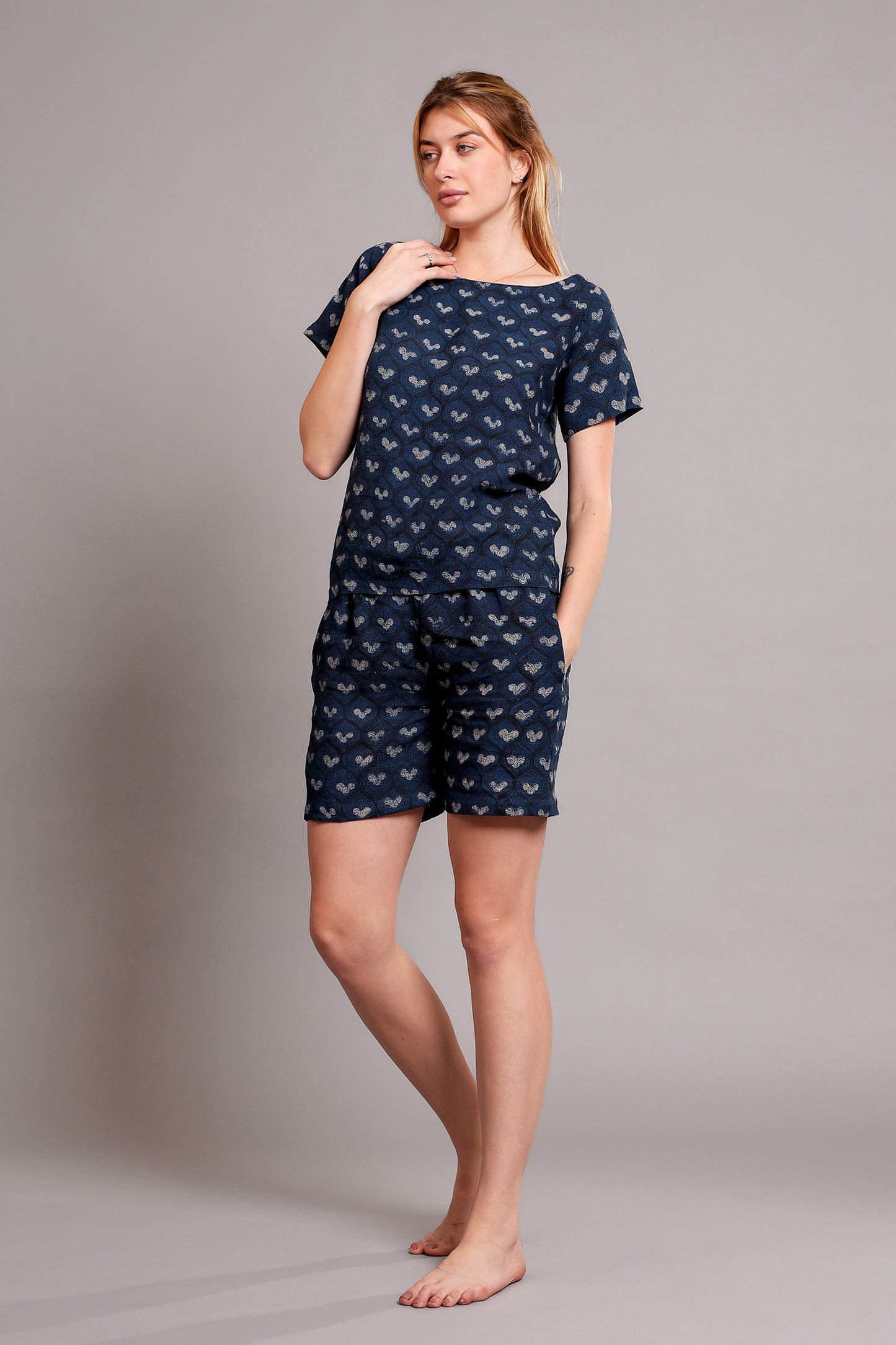 Woman wearing a navy blue patterned linen top and shorts pajama set against a gray background.