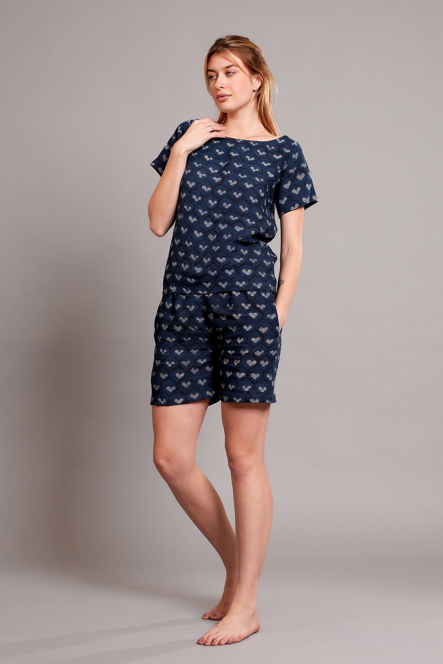 Woman wearing a navy blue patterned linen top and shorts pajama set against a gray background.