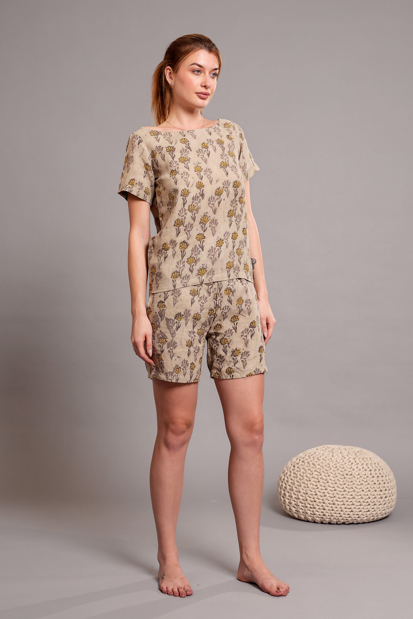Woman wearing a patterned linen floral top and shorts set standing against a gray background with a textured ball.