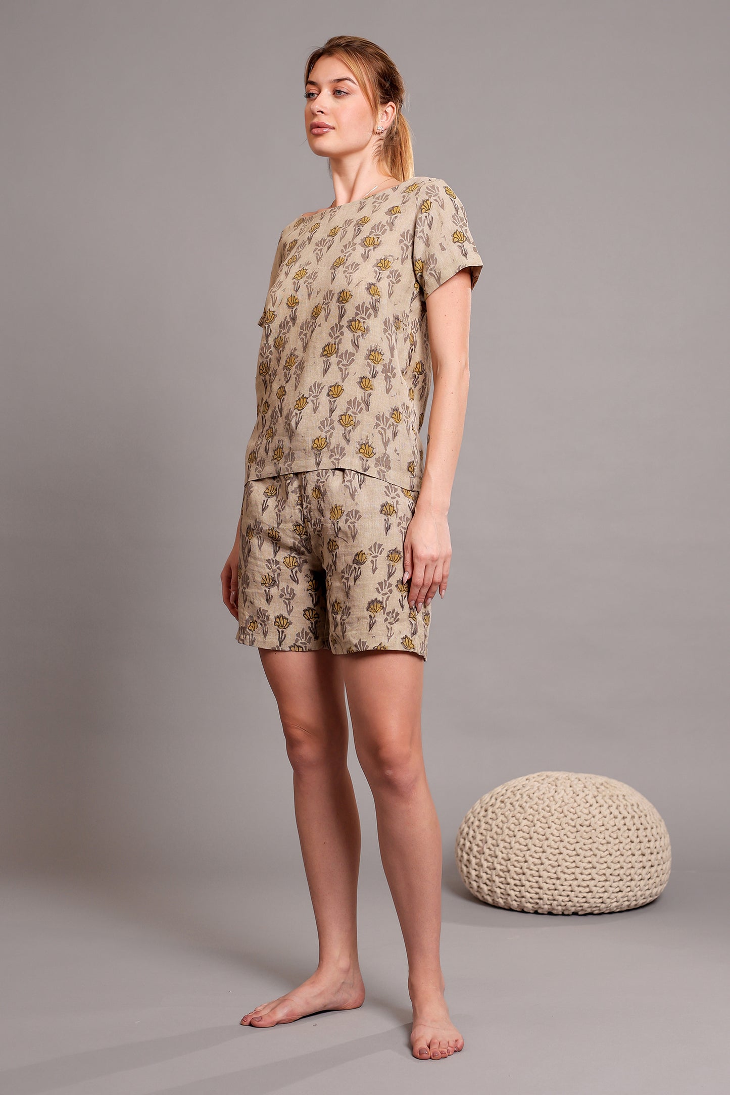 Woman wearing a linen floral top and shorts set against a gray background.
