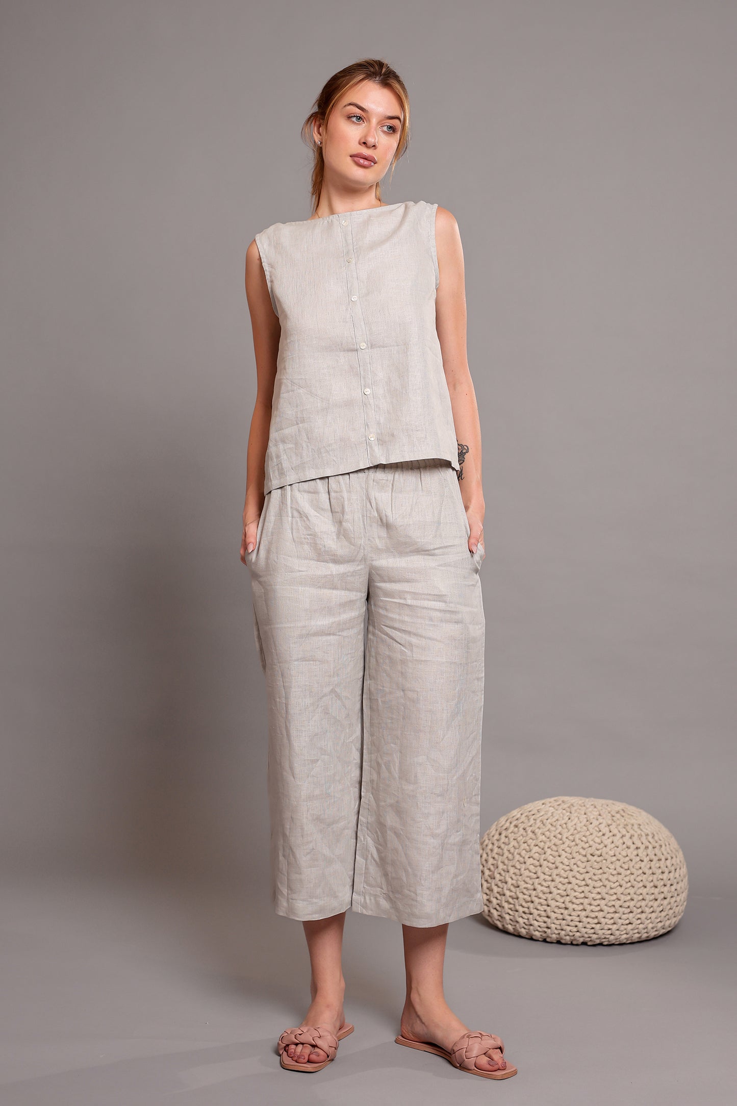Woman wearing a light gray linen sleeveless top with matching linen pants against a plain background.