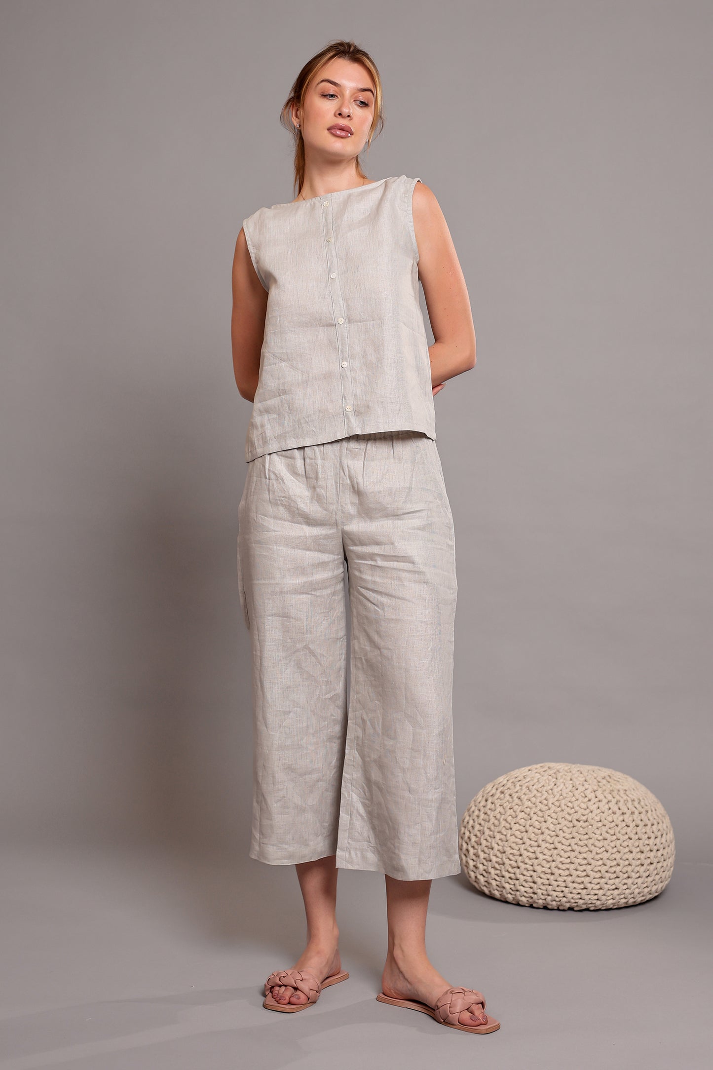 Woman wearing a light gray linen sleeveless top paired with linen pants standing against a plain background.
