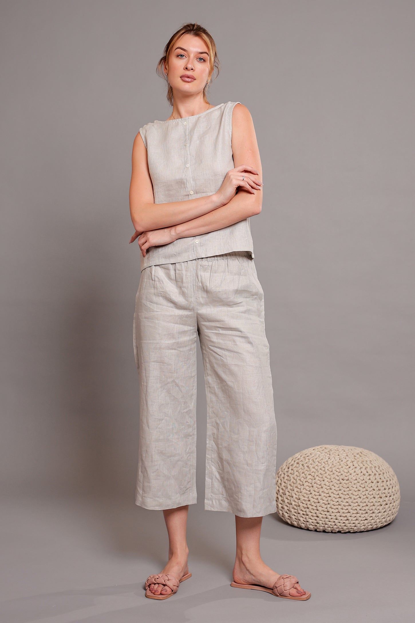 Woman wearing a light gray linen sleeveless top paired with linen pants standing against a plain background.
