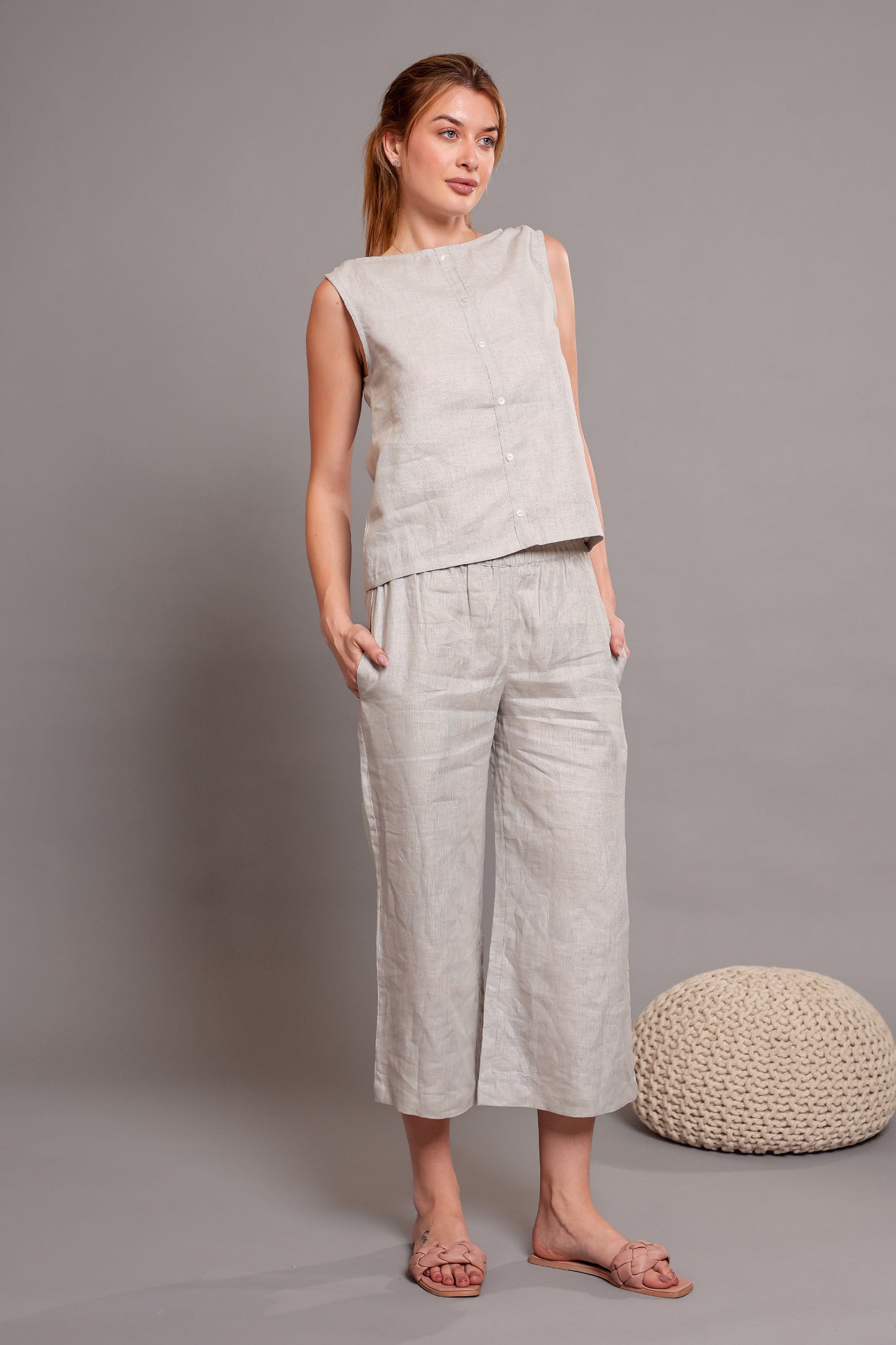 Woman wearing a light gray linen sleeveless top with matching linen pants standing against a plain background.