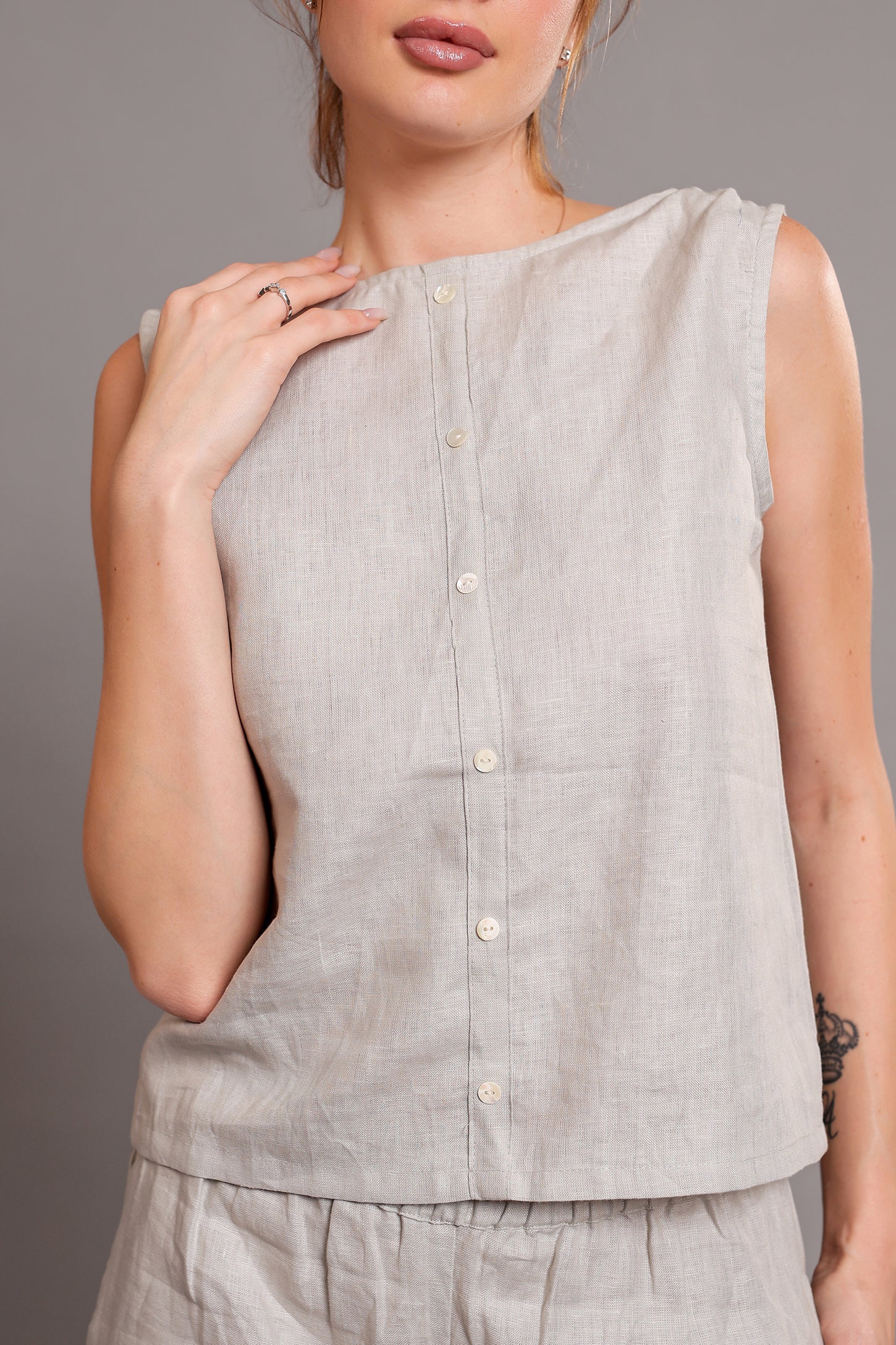 Woman wearing a light gray sleeveless linen top against a neutral background.