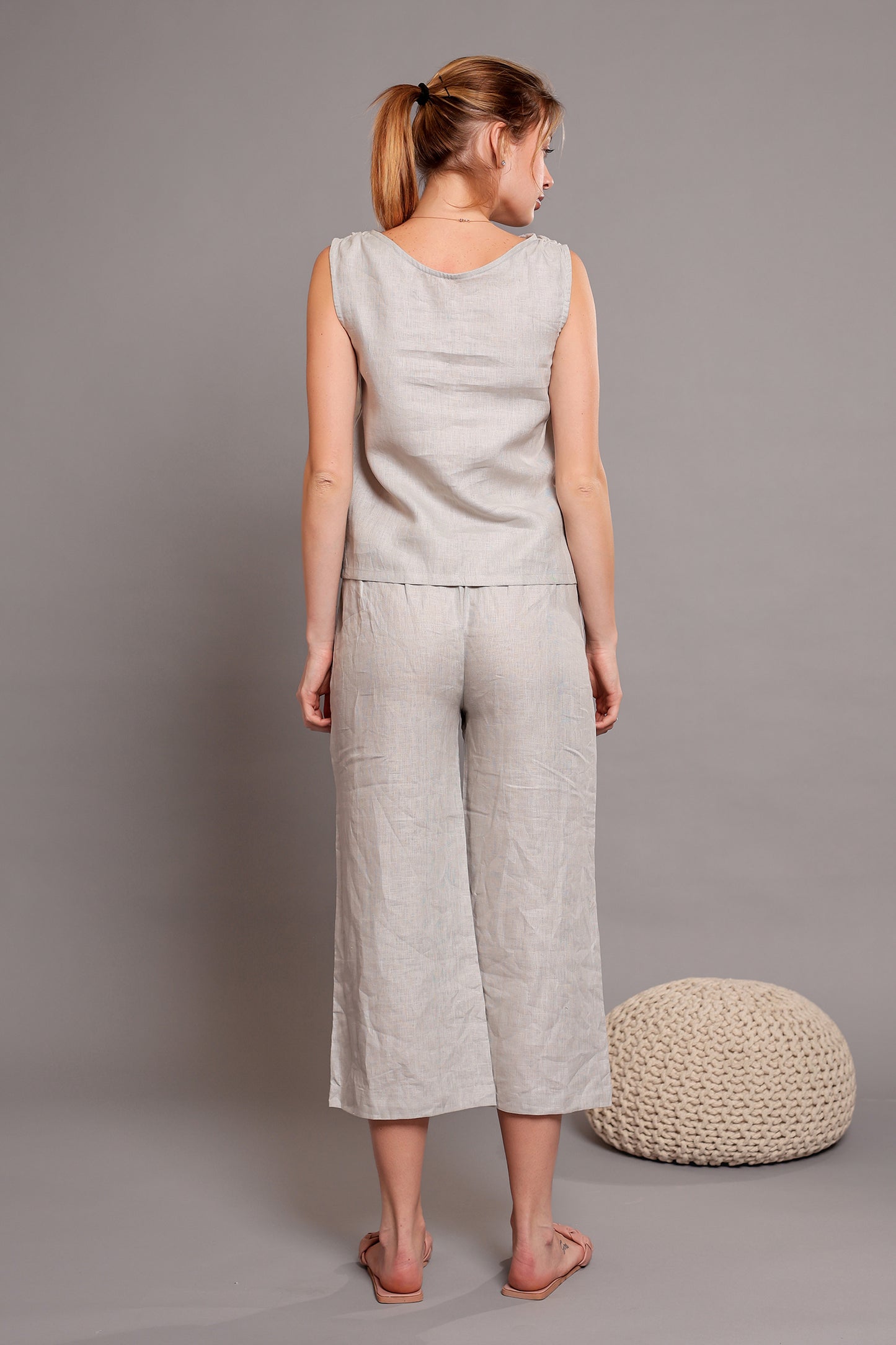Woman wearing a light gray sleeveless linen top with matching linen pants against a plain background.