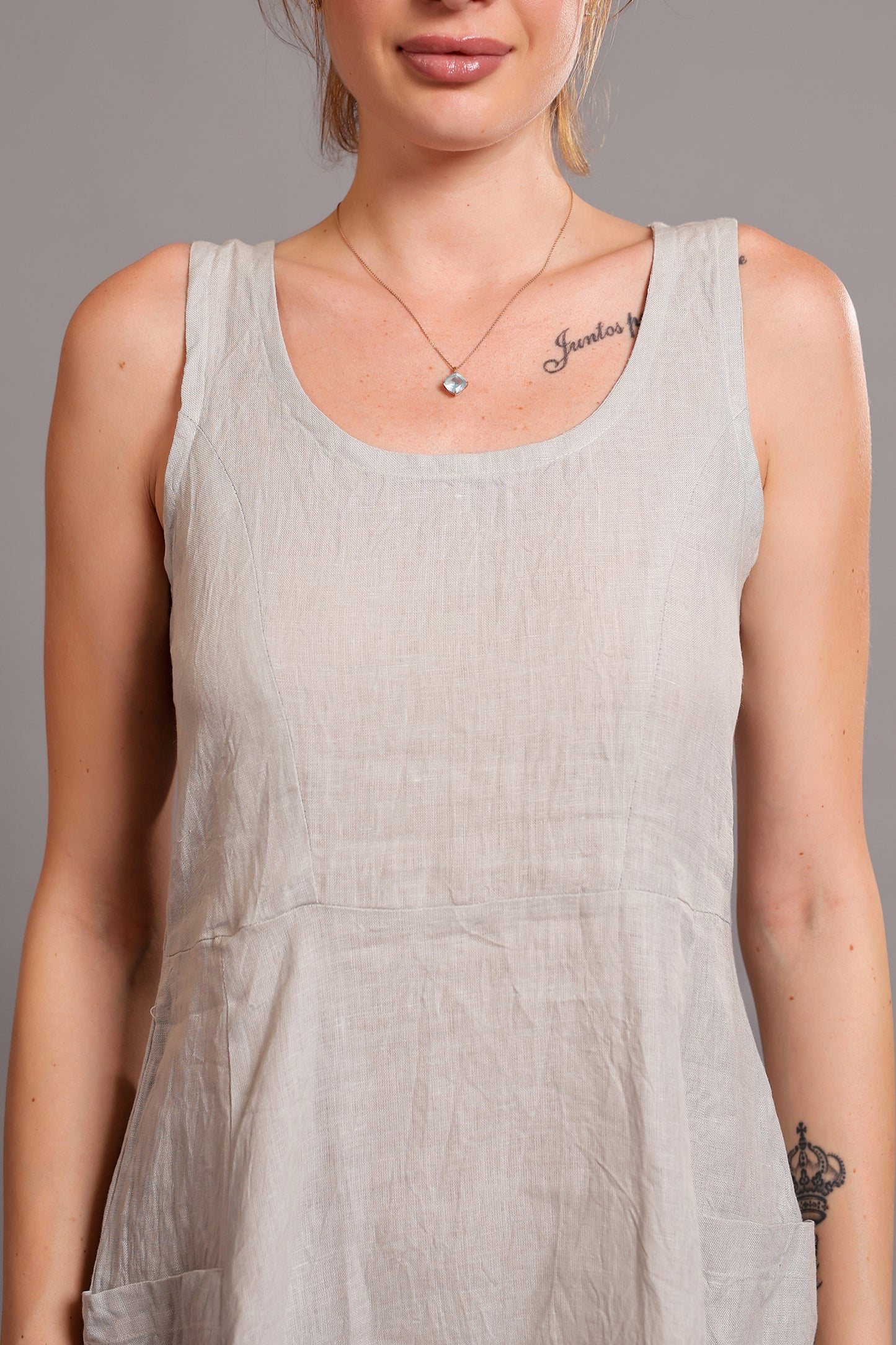 Woman wearing a light gray sleeveless linen midi dress against a neutral background.