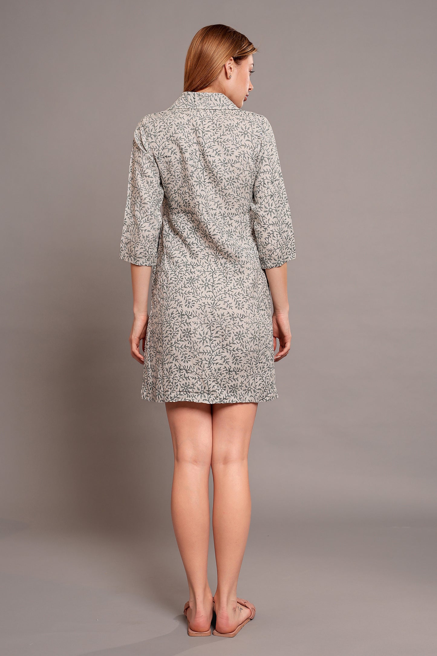 Woman wearing a linen floral dress against a plain background.