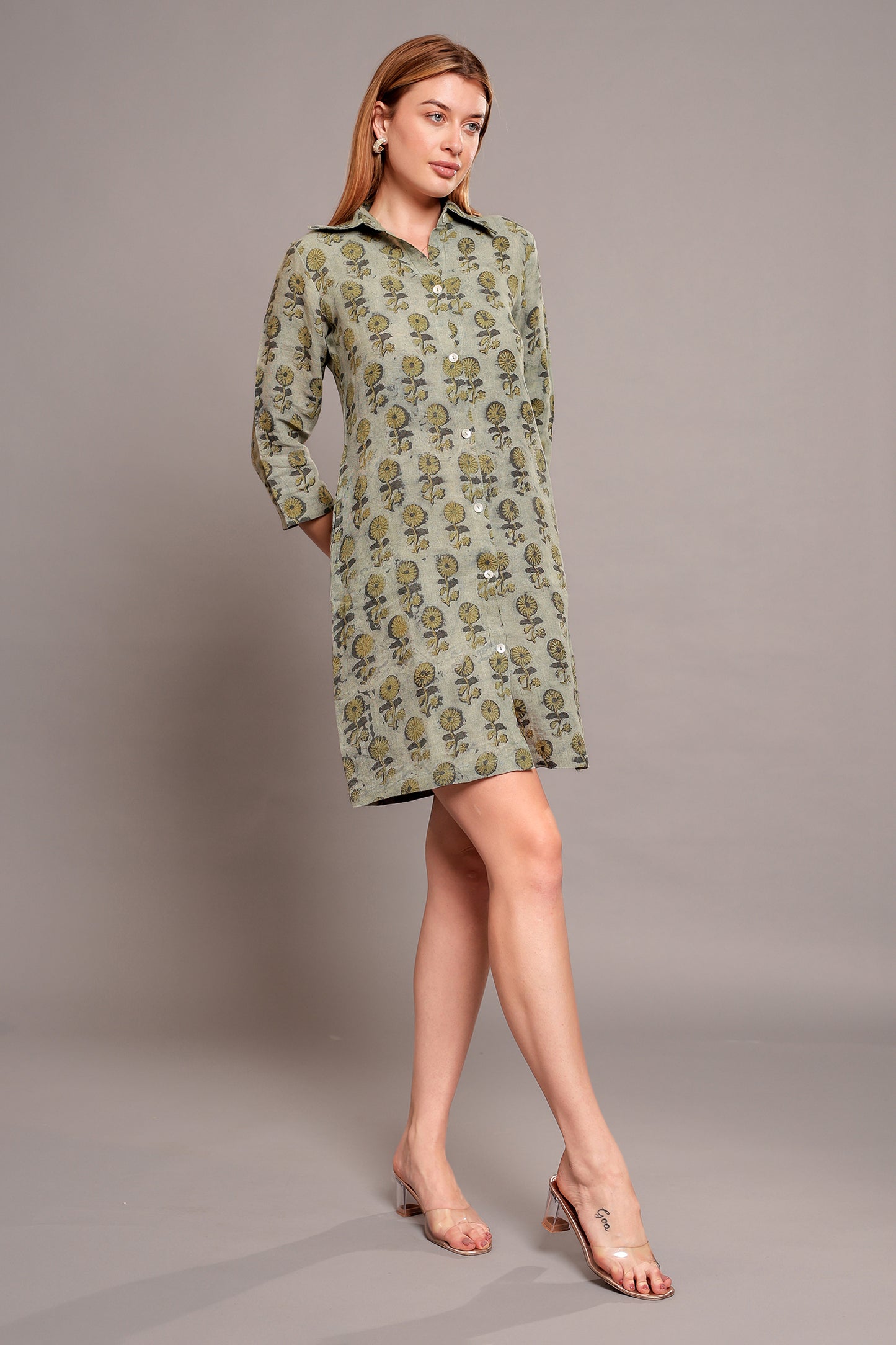 Woman wearing a green patterned linen mini dress against a gray background.
