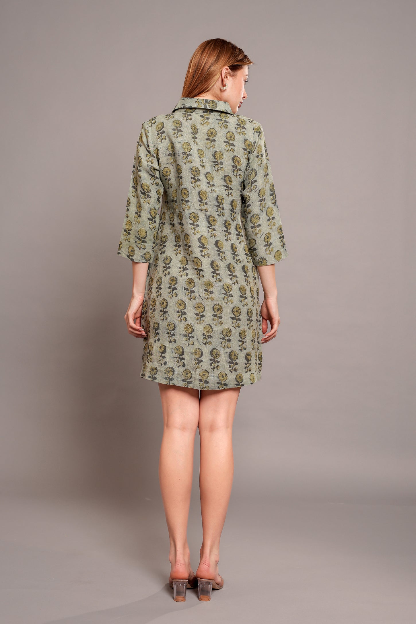 Woman wearing a green patterned linen mini dress against a gray background.